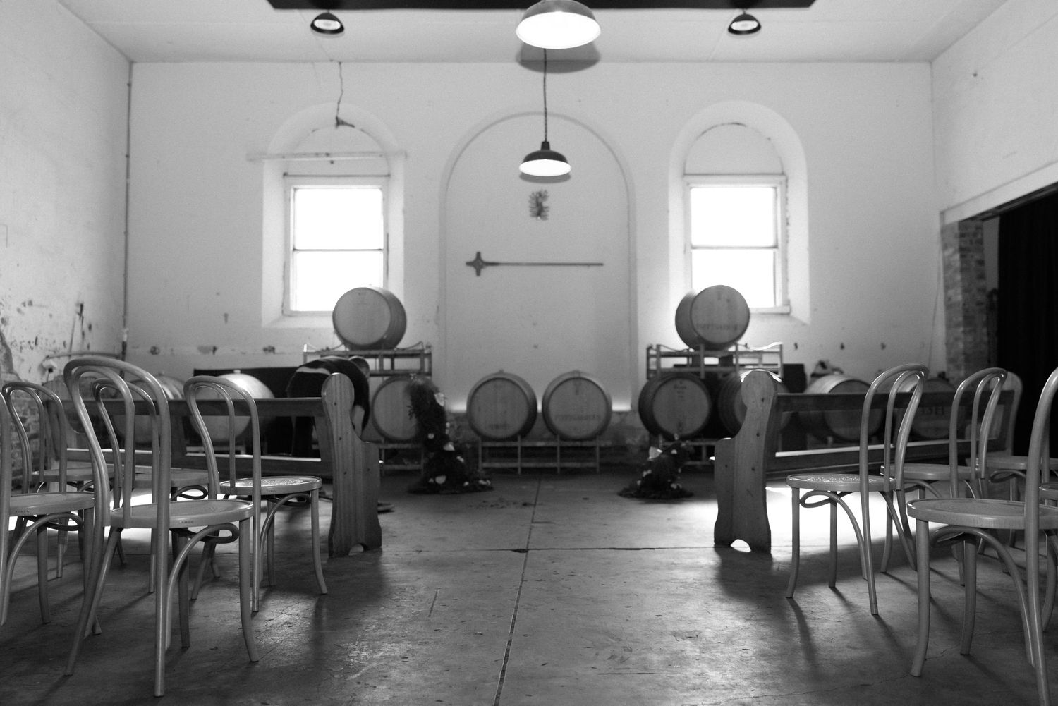 Black and white image of rustic winery ceremony space with oak barrels, bentwood chairs and arched windows.