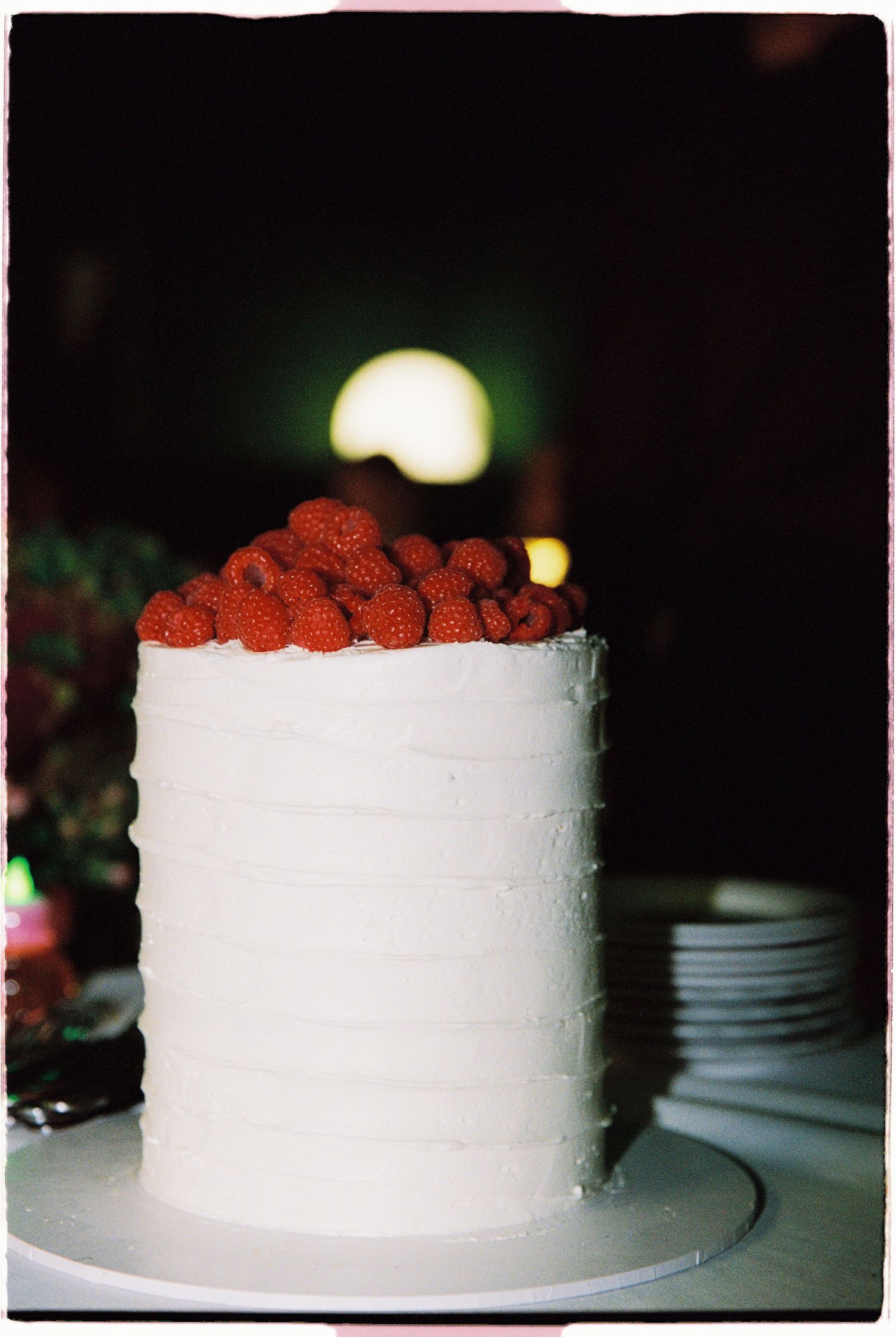 Elegant white frosted layer cake topped with fresh red raspberries on a white cake stand.