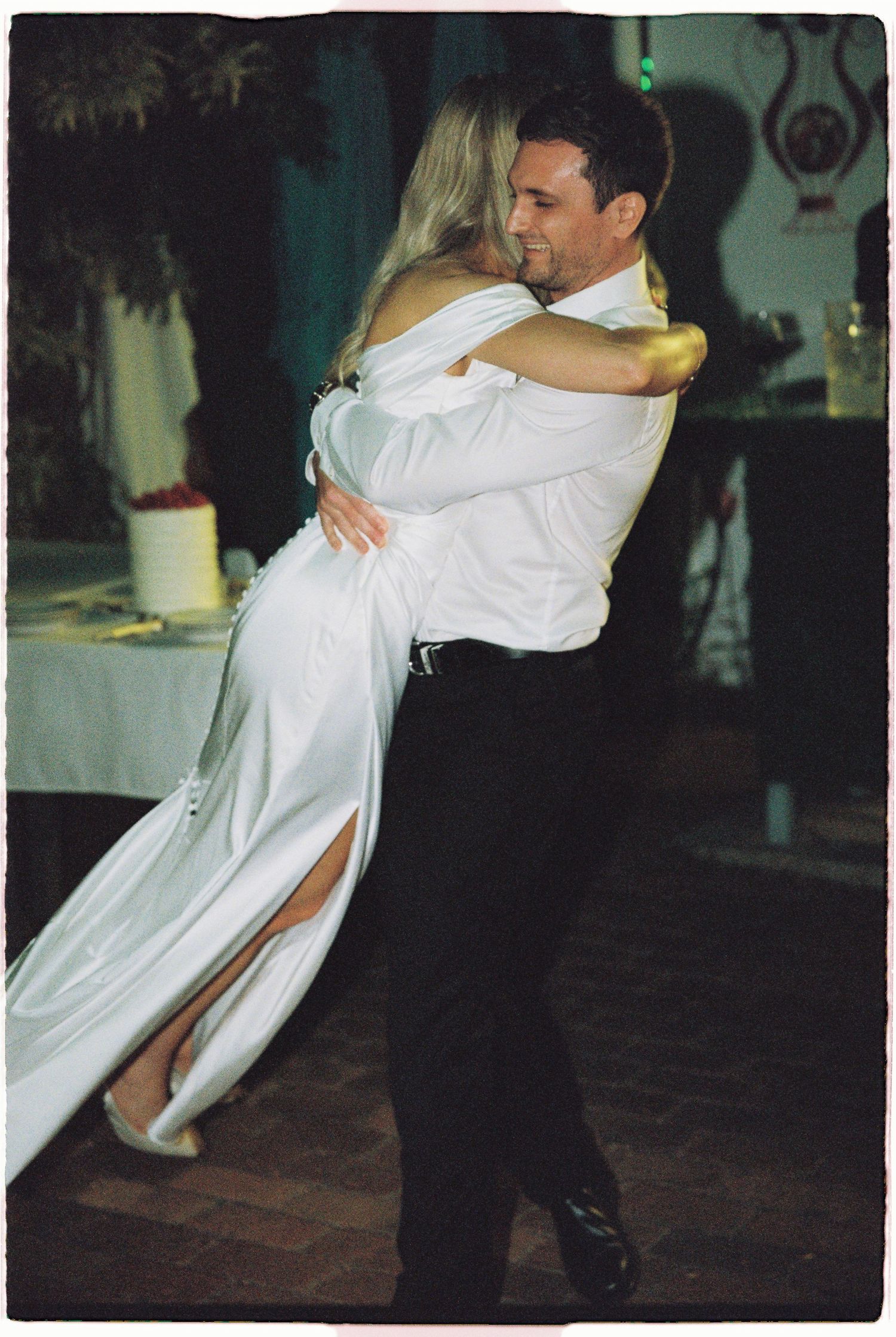 Groom lifts bride in white off-shoulder gown during romantic first dance.