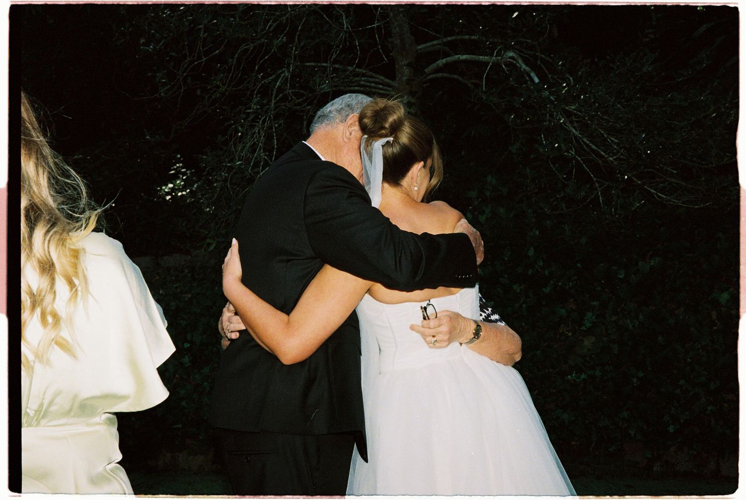 Bride and father sharing an emotional hug during wedding ceremony outdoors at night.