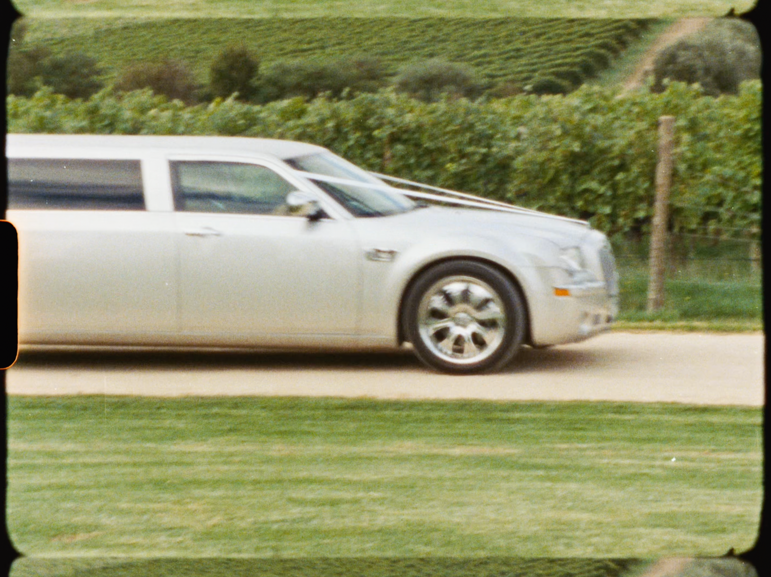 Silver stretch limousine driving along a vineyard road at a wedding venue.