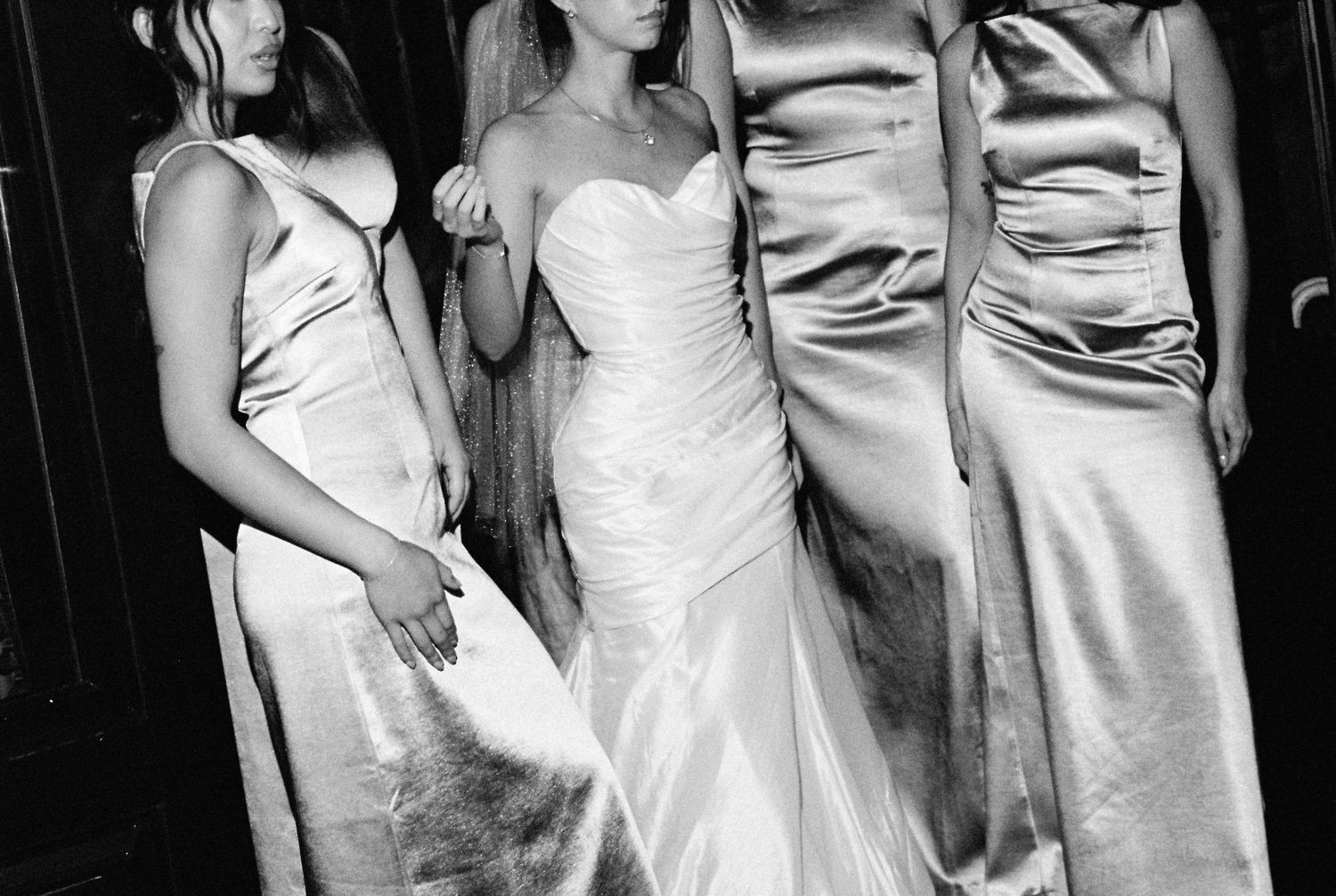 Bride in strapless mermaid gown surrounded by bridesmaids in silver satin dresses.