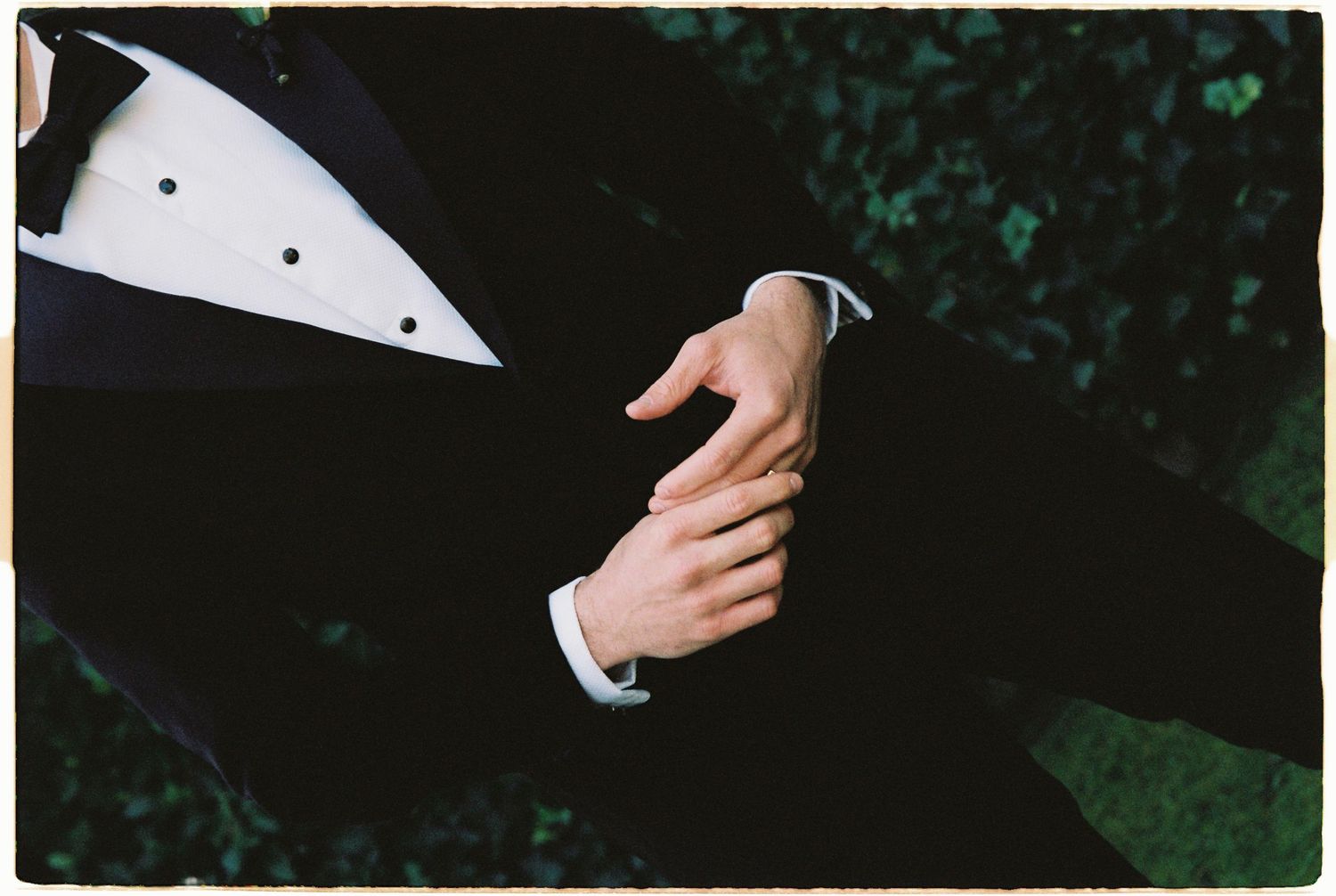 Two people in formal tuxedos holding hands, showcasing elegant black suits with white dress shirts.