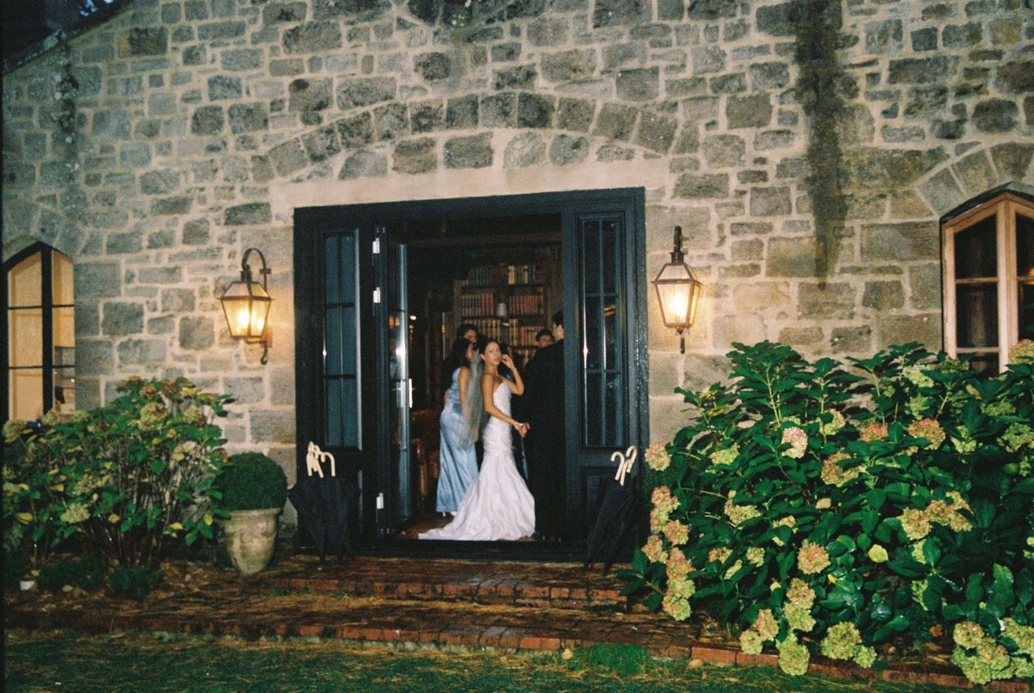 Bride and groom kissing in doorway of stone building with lanterns at night.