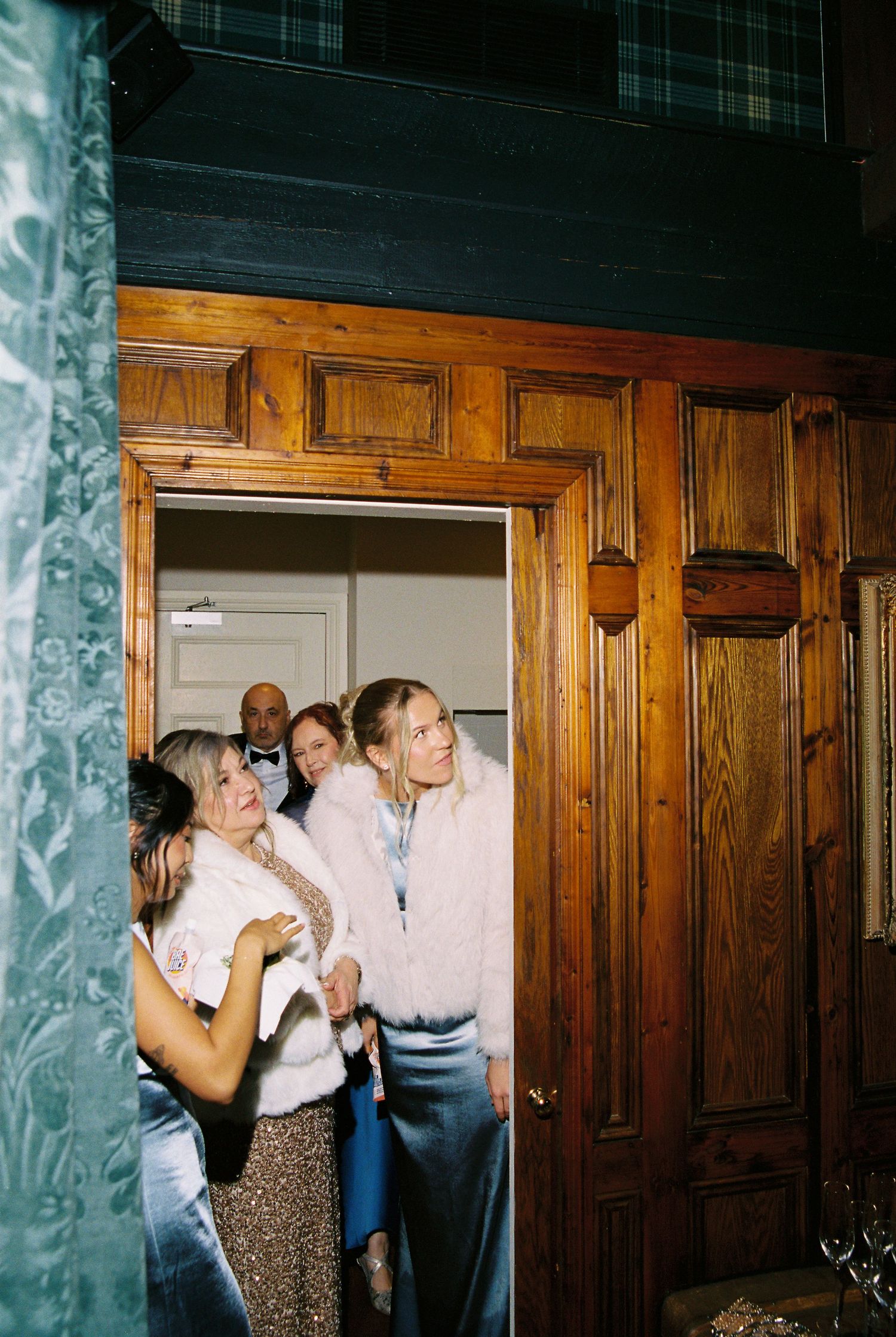 Wedding guests gathering at wooden doorway inside rustic venue during reception celebration.