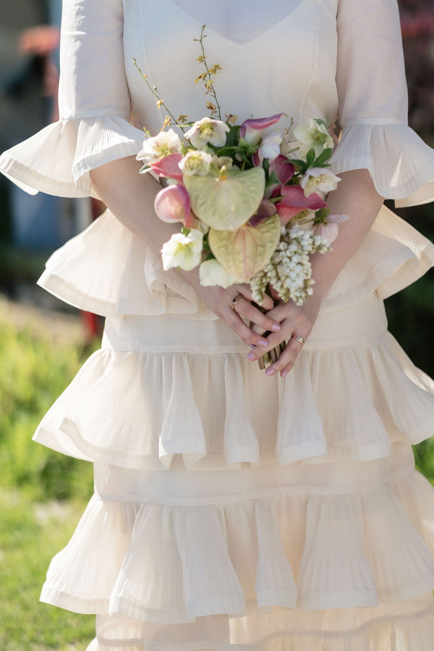 Bride in tiered cream ruffle dress holding elegant bouquet of pink tulips, anthurium and lily of the valley.