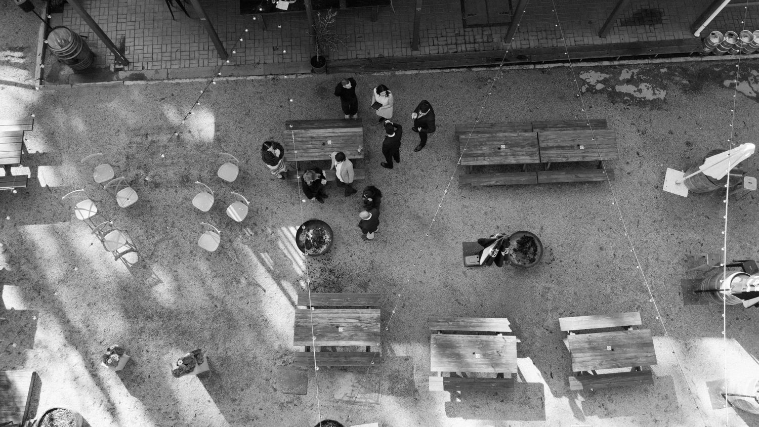 Aerial black and white photo of people gathering in an urban plaza with benches and paved ground.