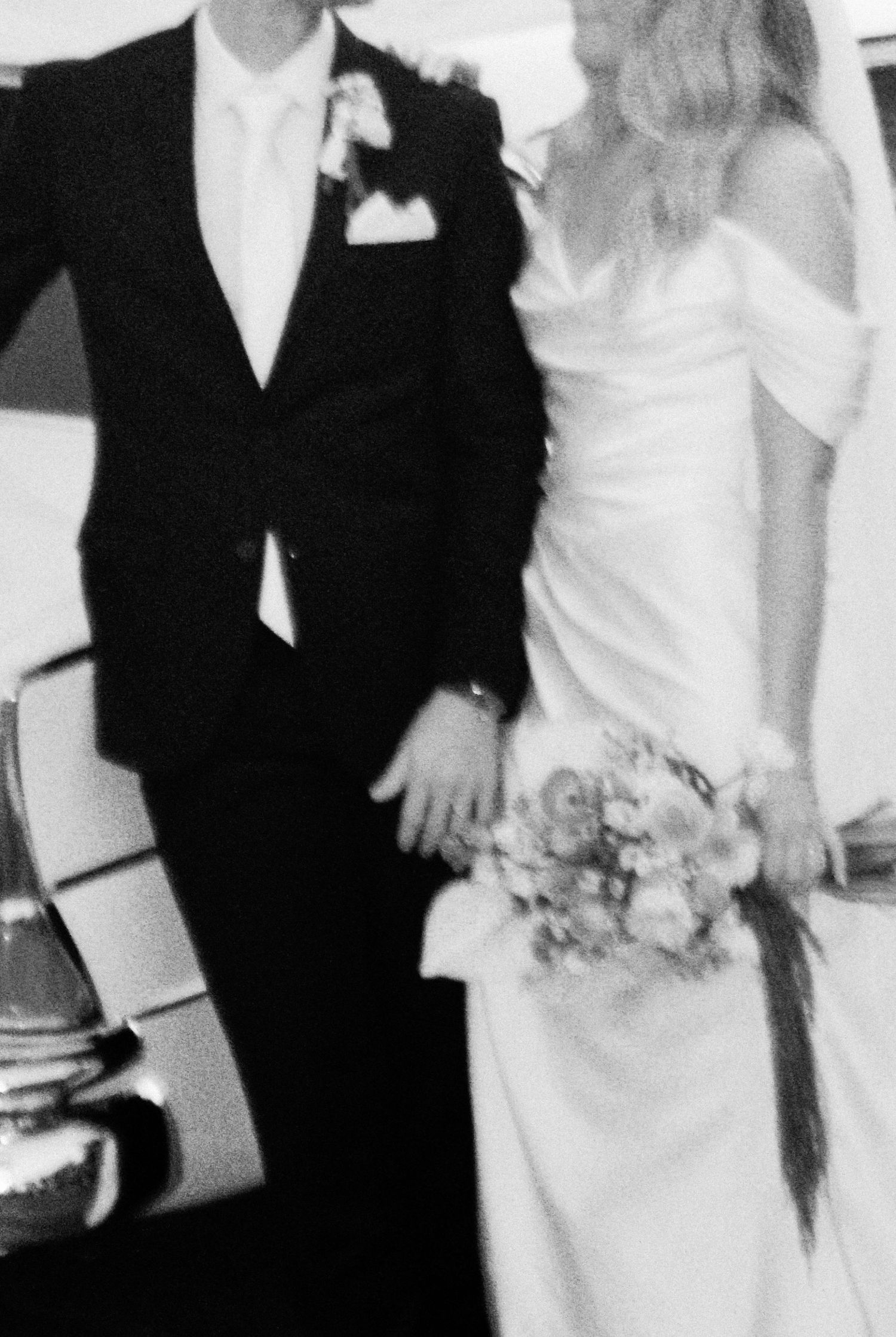 Bride and groom walking hand in hand in elegant black and white wedding photo.