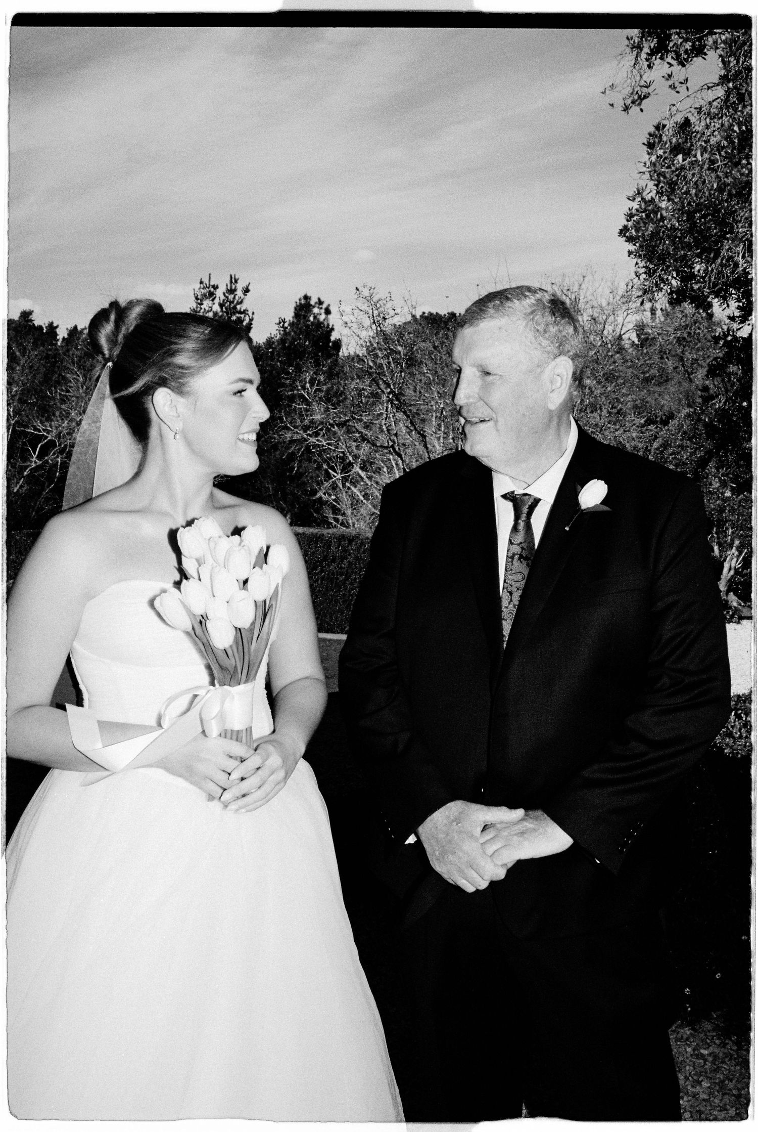 Black and white wedding photo of a smiling bride holding tulips standing beside a man in a suit with a boutonniere.