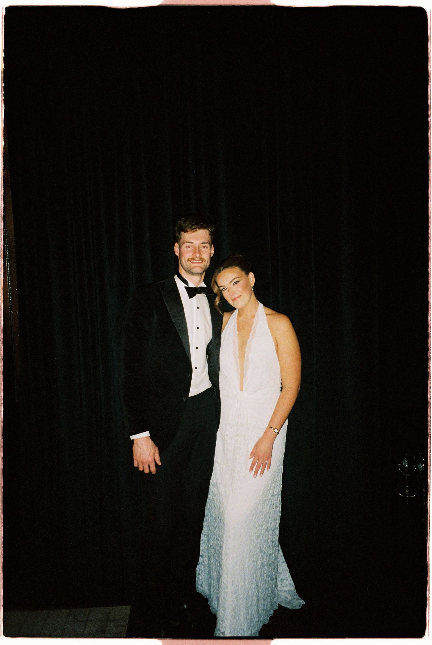 Couple in formal wedding attire posing together in front of a black curtain backdrop.