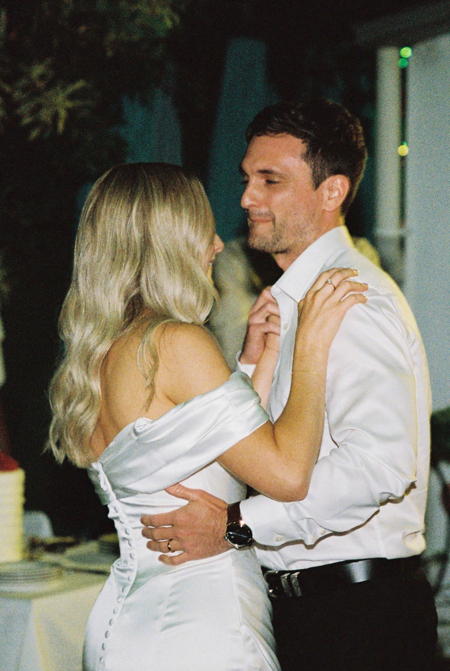 Bride and groom sharing intimate first dance outdoors at night, bride in white satin gown.