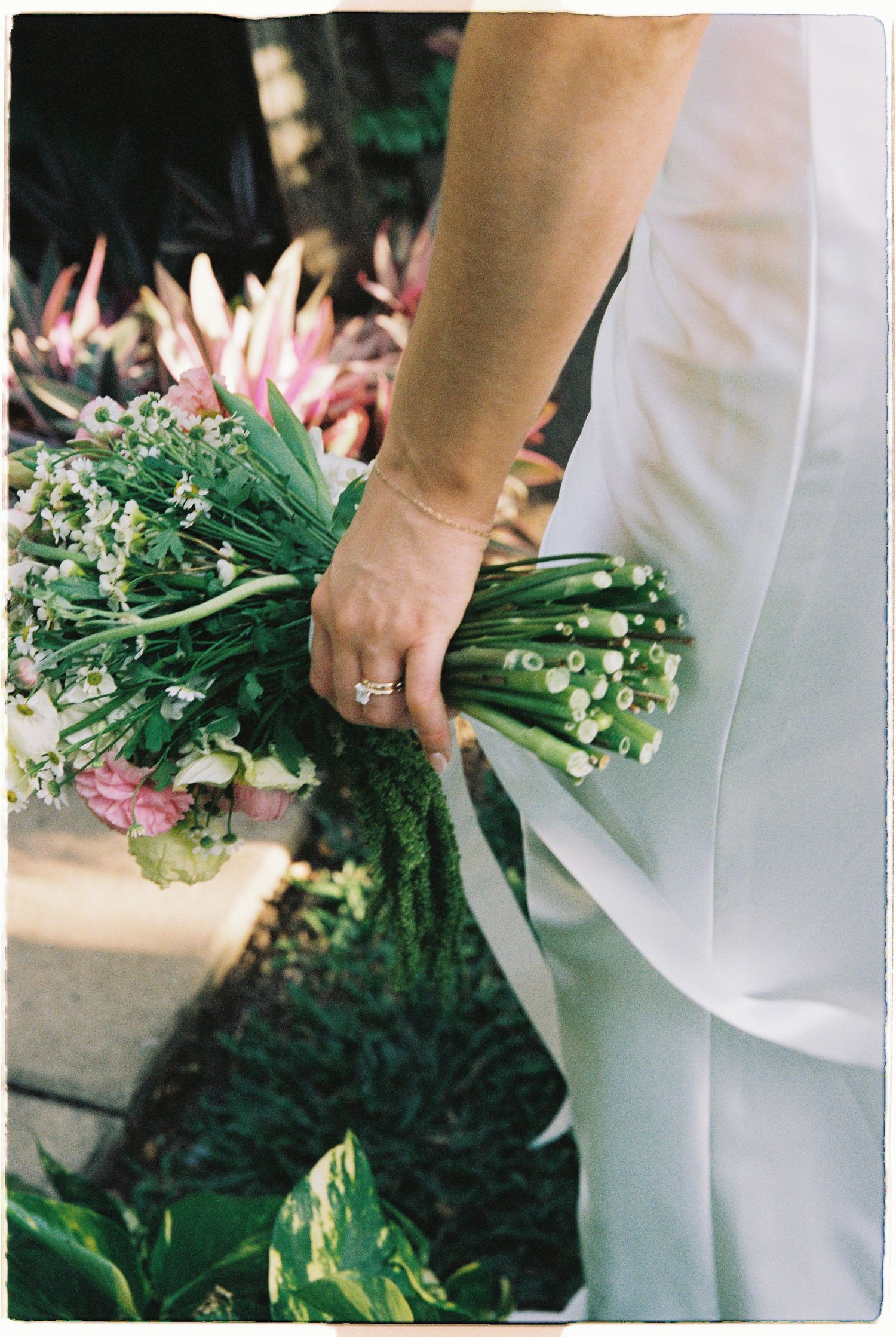 A bride holds a lush green and pink floral bouquet with a diamond ring on her finger.