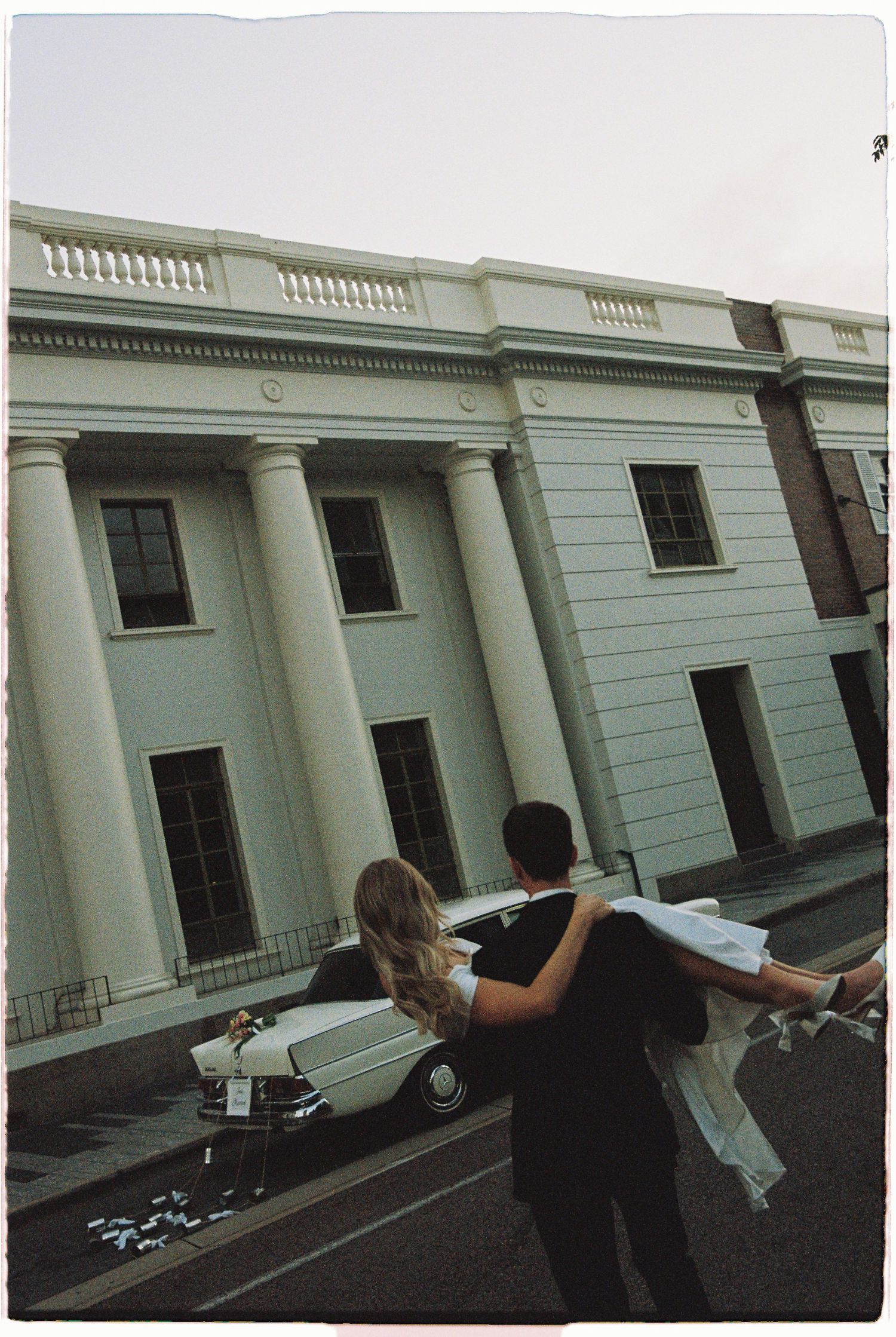 Groom sweeps bride off her feet outside a stunning white columned building on their wedding day.