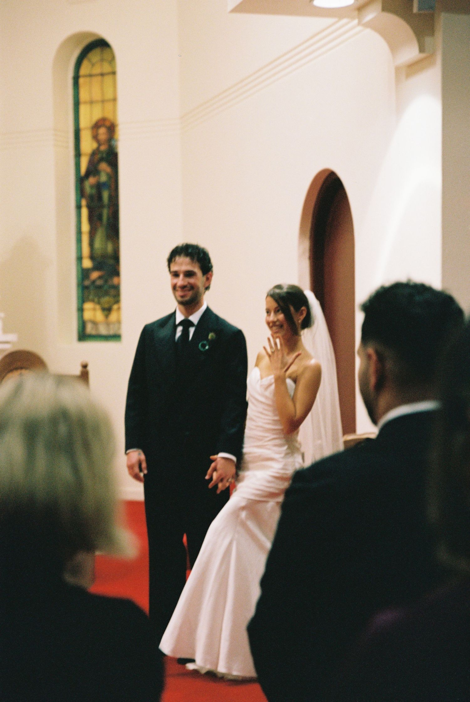 Newlywed couple holding hands and smiling at the altar inside a church with stained glass windows during their wedding ceremony.