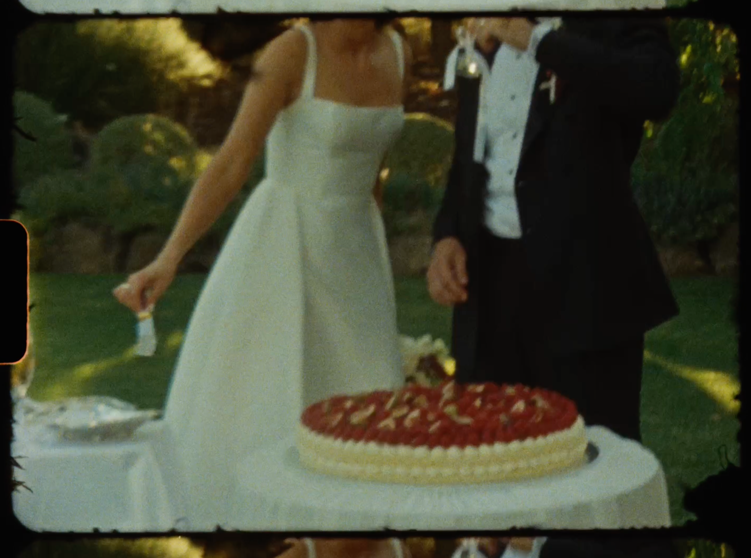 Close-up of bride and groom cutting a red and white decorated wedding cake at outdoor reception.