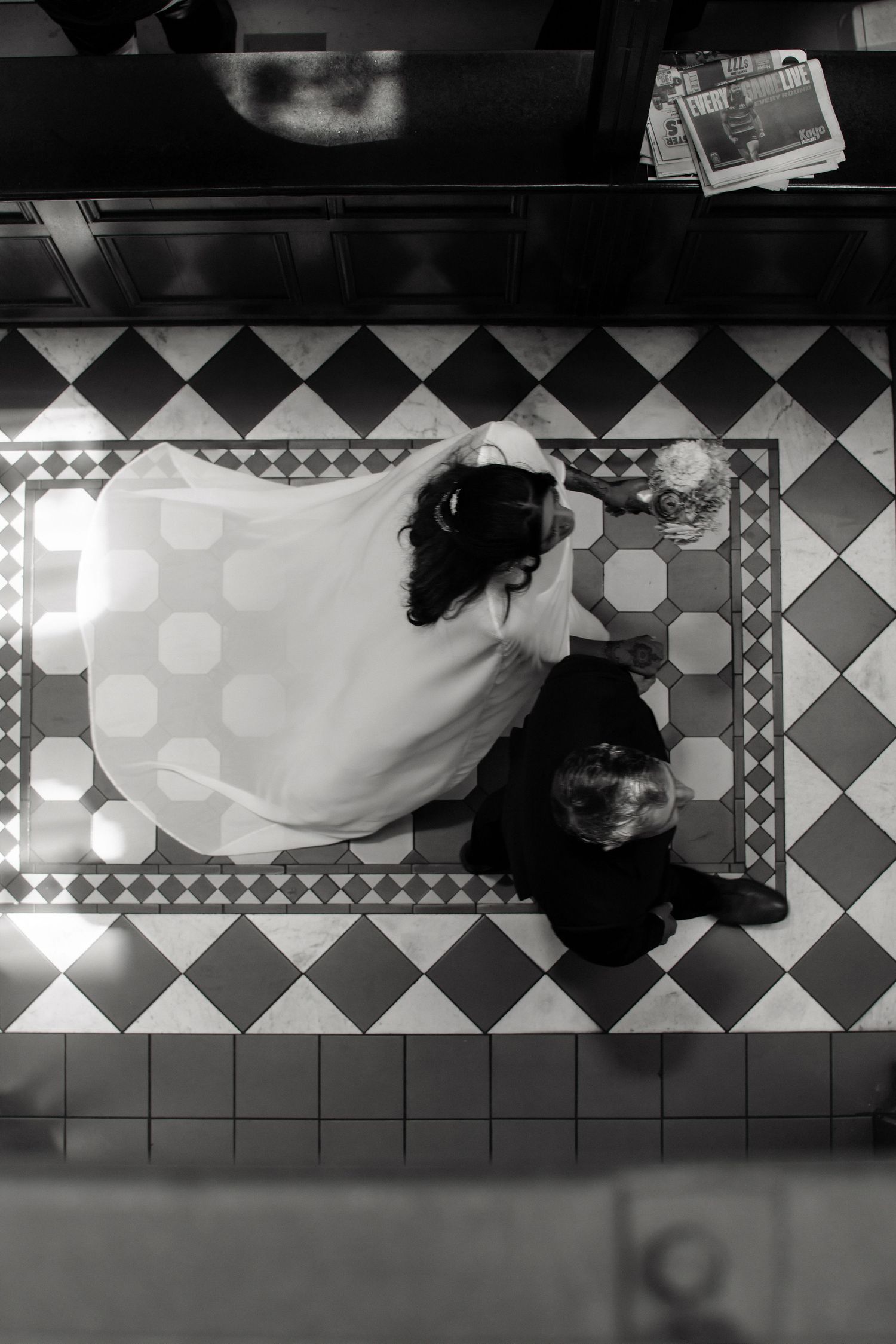Aerial black and white photo of bride and groom embracing on classic geometric tiled floor.