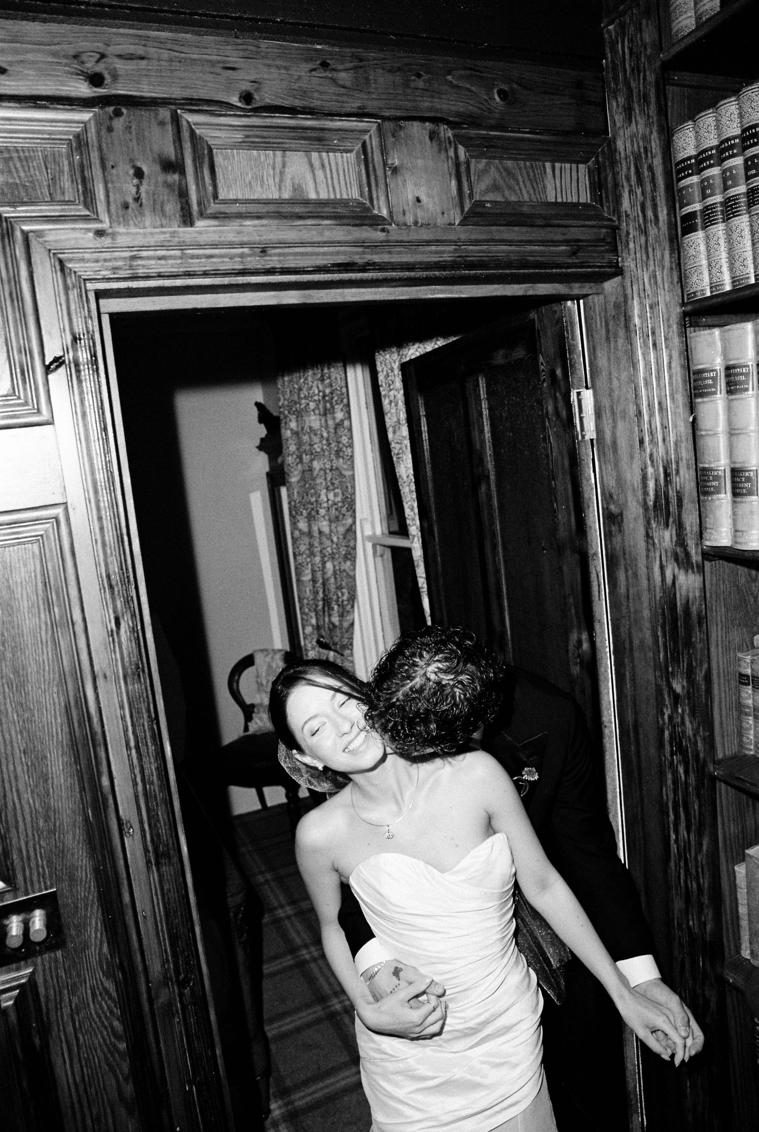 Bride in strapless white gown laughing joyfully in rustic wood-paneled doorway.