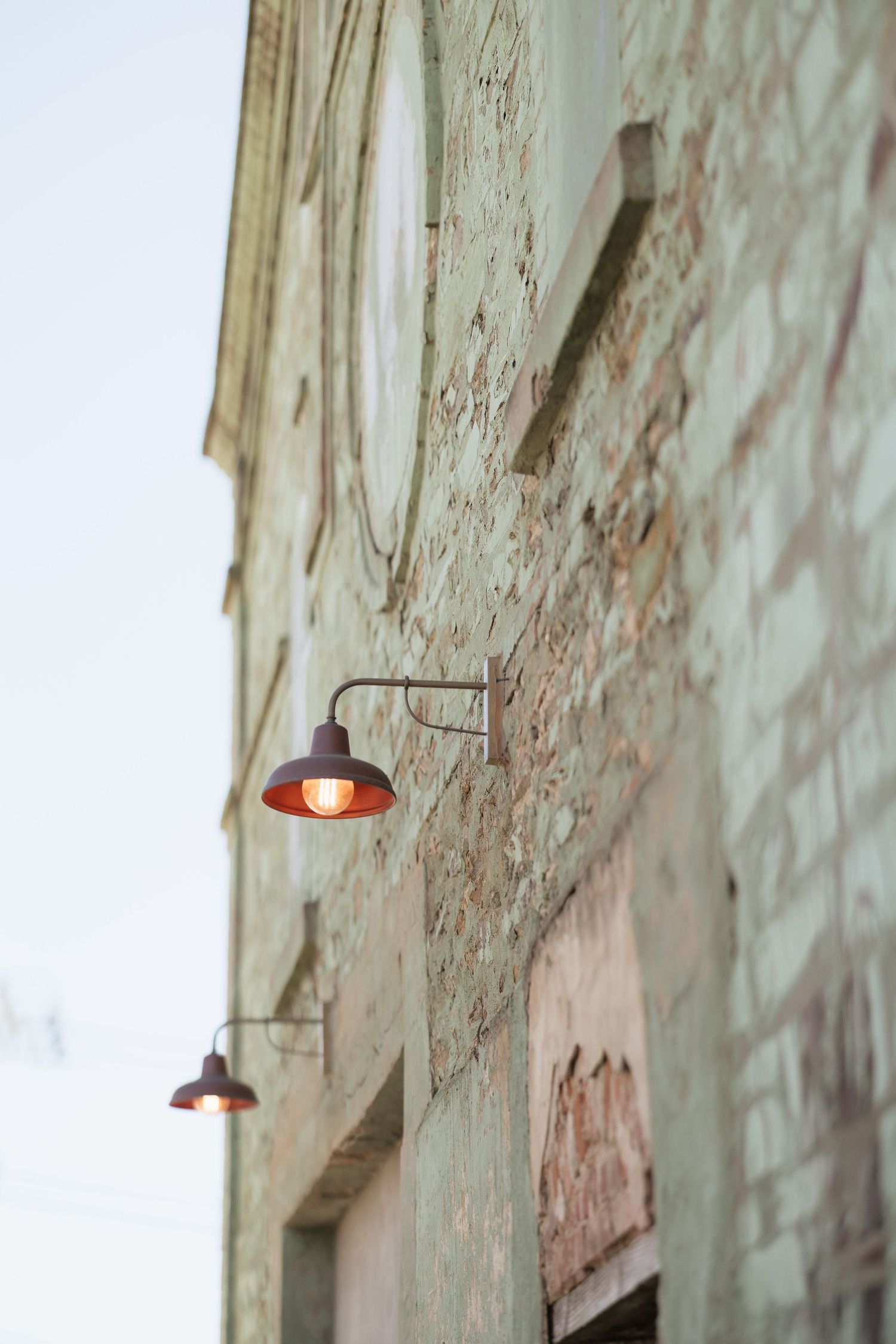 Vintage brick building exterior with glowing antique wall-mounted lanterns at dusk.