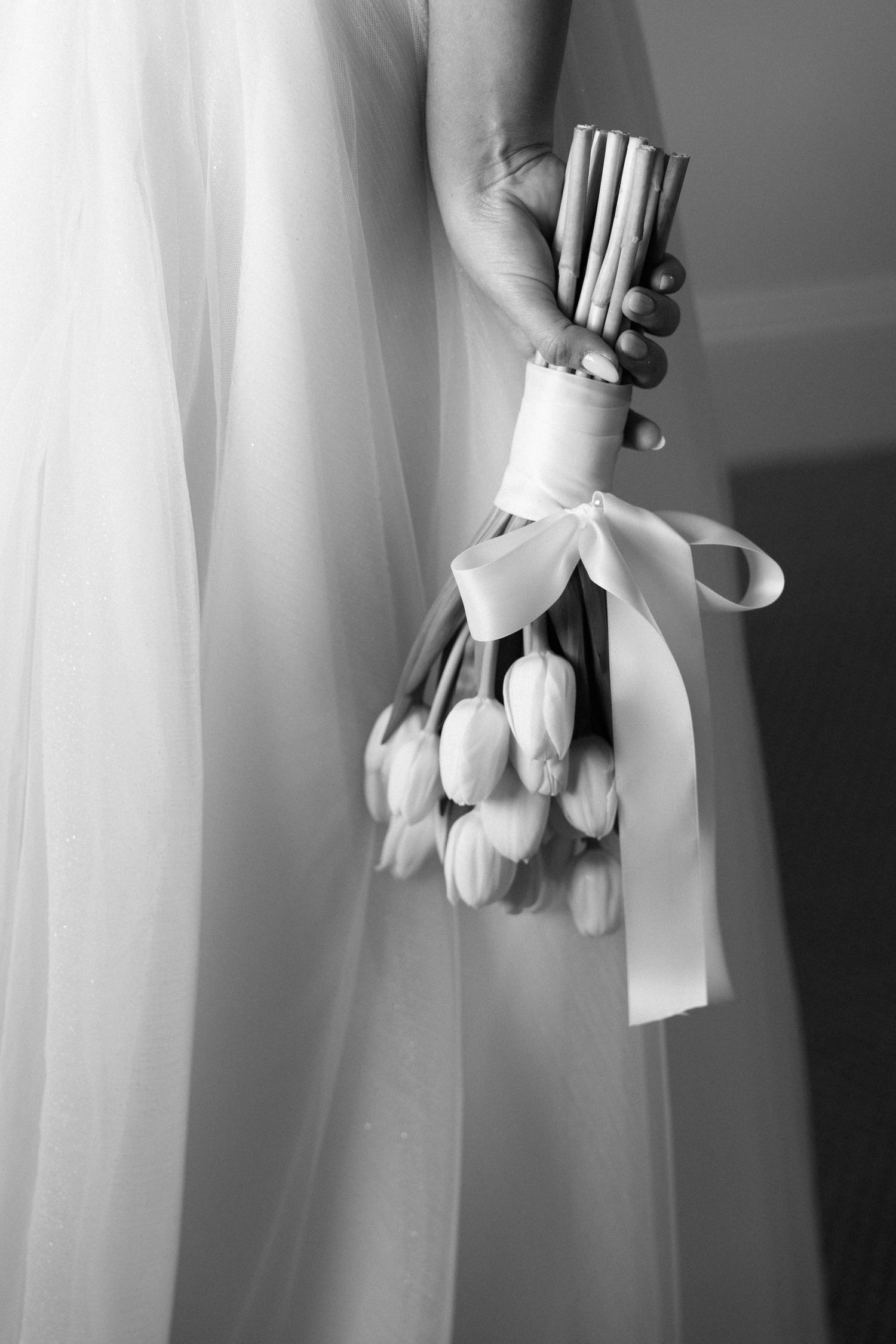 Black and white close-up of bride holding a white tulip bouquet tied with a satin ribbon bow.