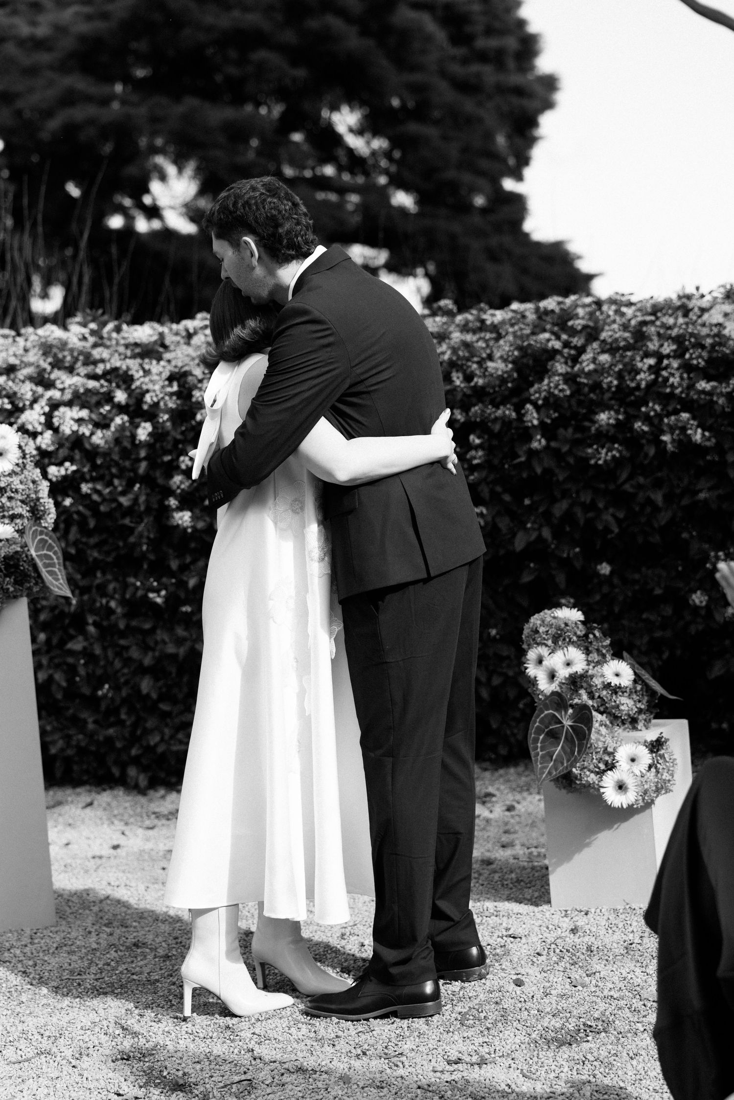 Black and white photo of a bride and groom sharing a tender embrace during their outdoor wedding ceremony.