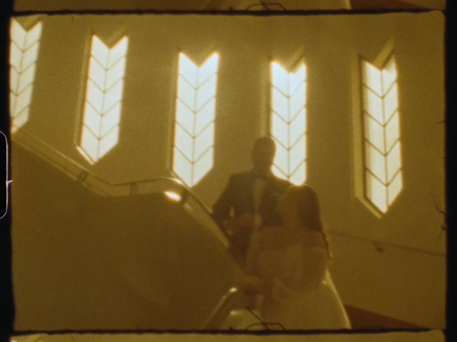 Silhouetted couple on staircase with ornate stained glass windows glowing warmly in background.