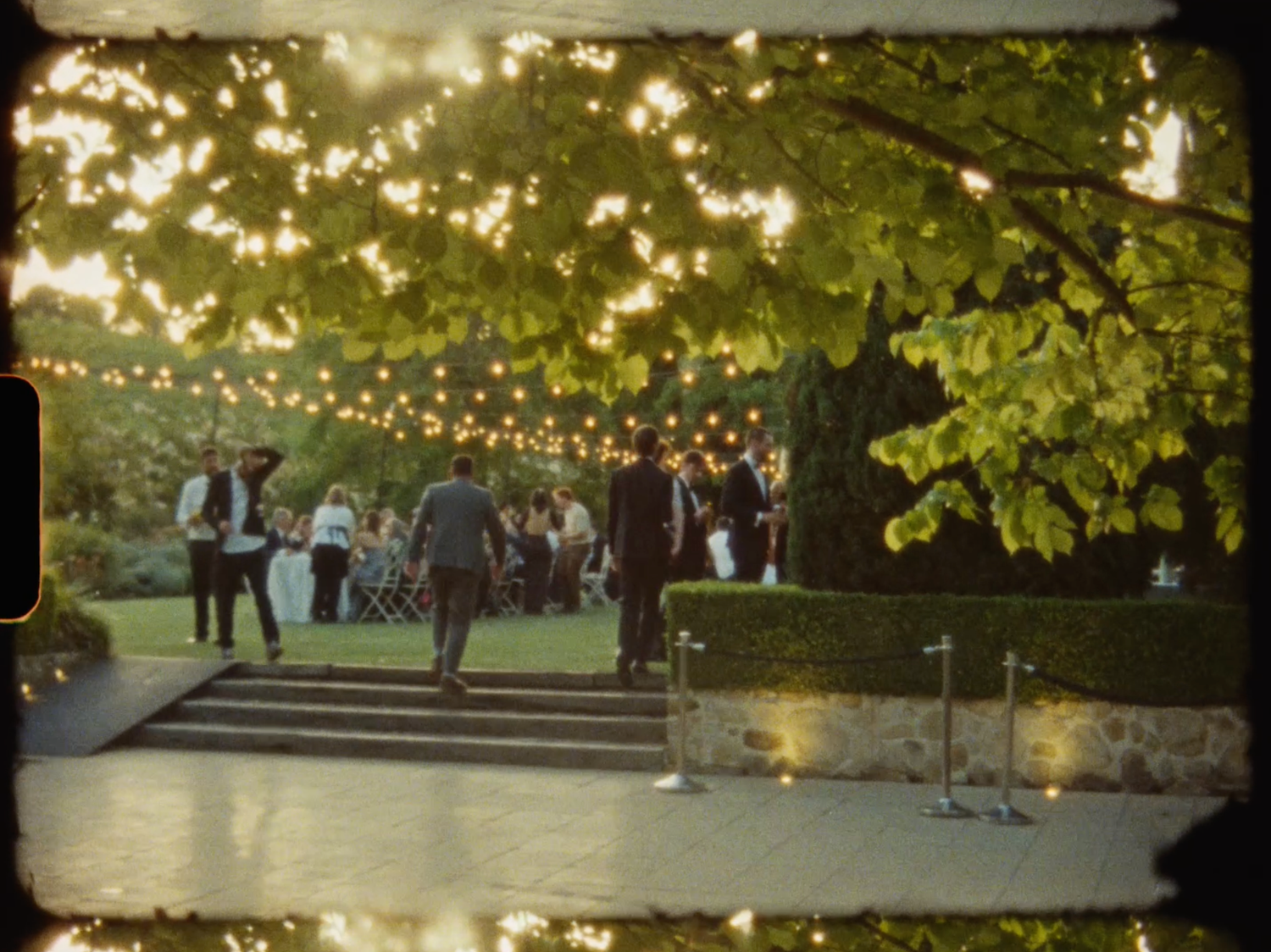 Wedding guests gather on stone steps under warm string lights at dusk.
