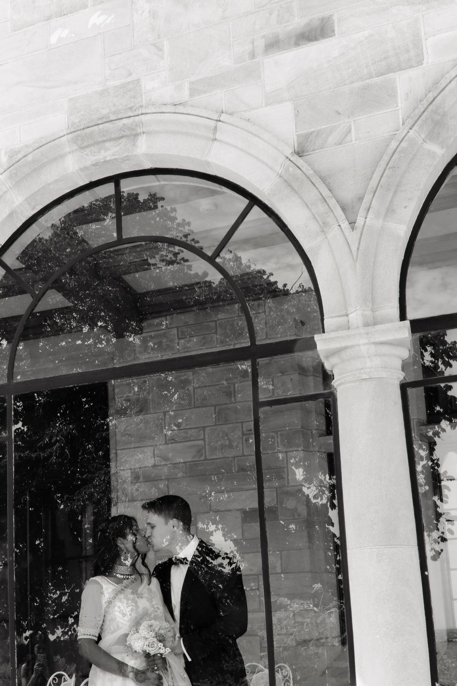 Bride and groom share intimate moment under arched windows of a stone building.