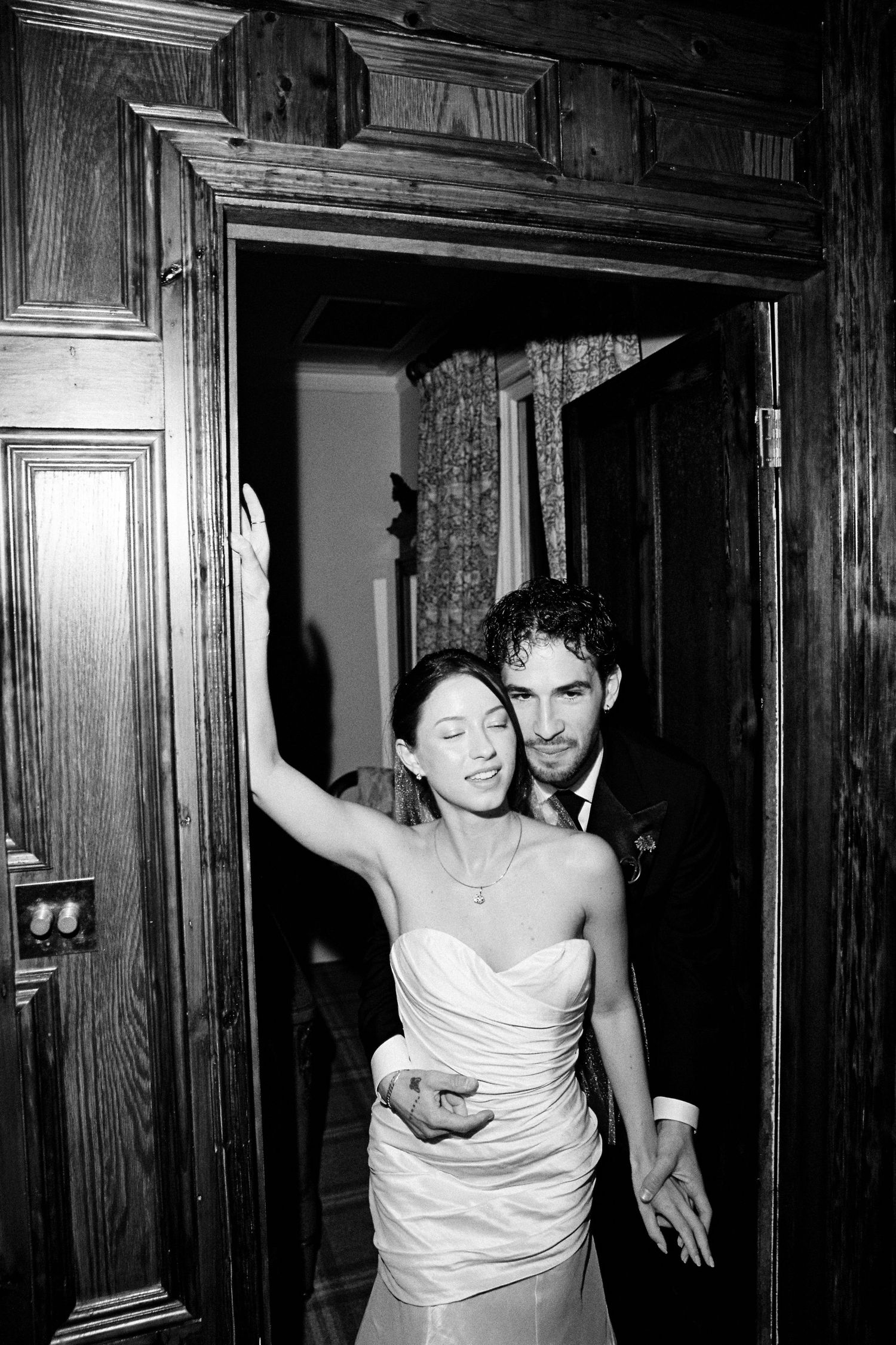 Bride and groom embracing in doorway, smiling, black and white wedding portrait.