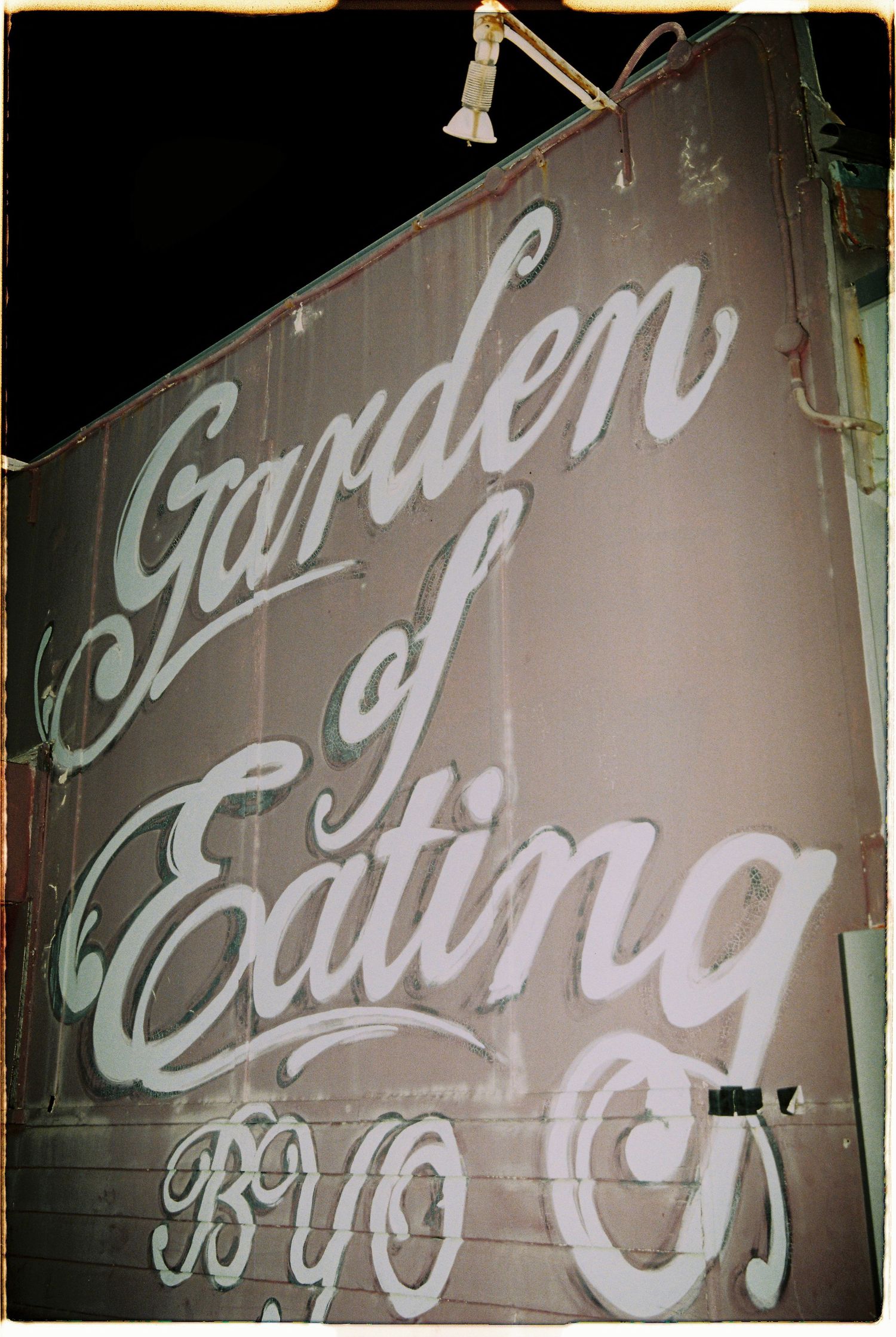 Vintage Garden of Eating BYO restaurant sign painted in white cursive script on dark wall.