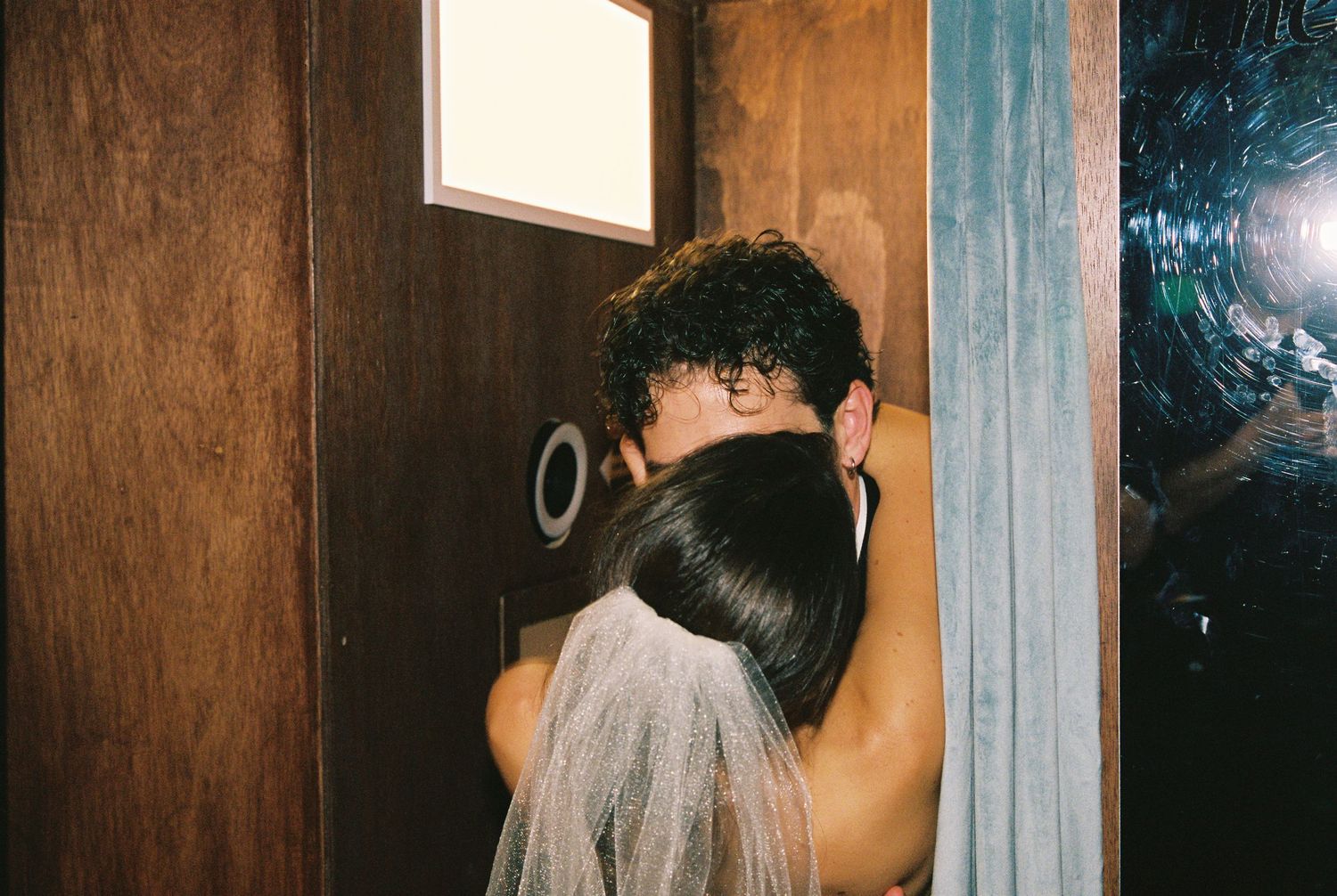 Bride and groom share intimate embrace in doorway, wedding veil visible.