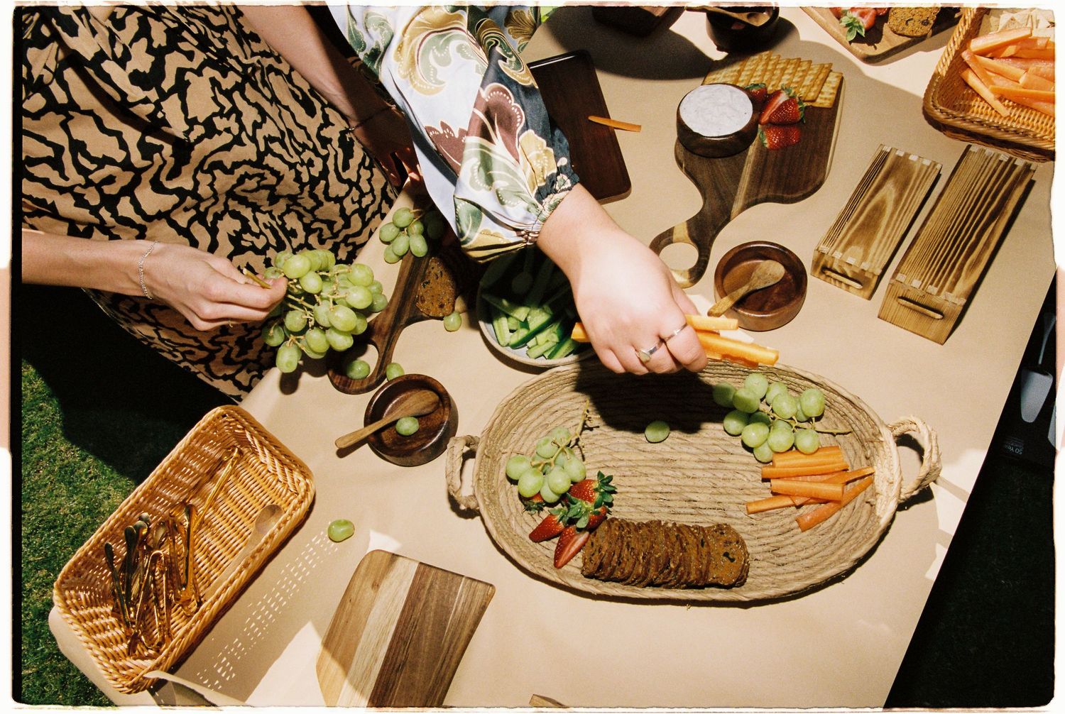 Overhead view of a grazing board with grapes, carrots, crackers, and dips on an outdoor table.