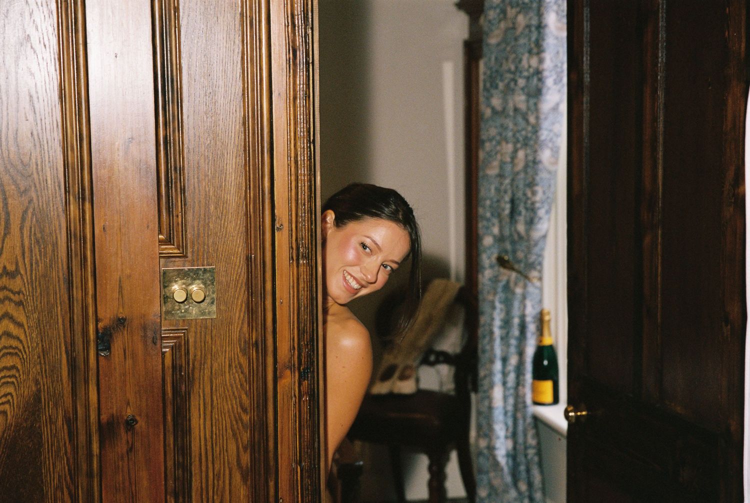 Smiling bride peeks through a slightly open ornate wooden door before her wedding ceremony.