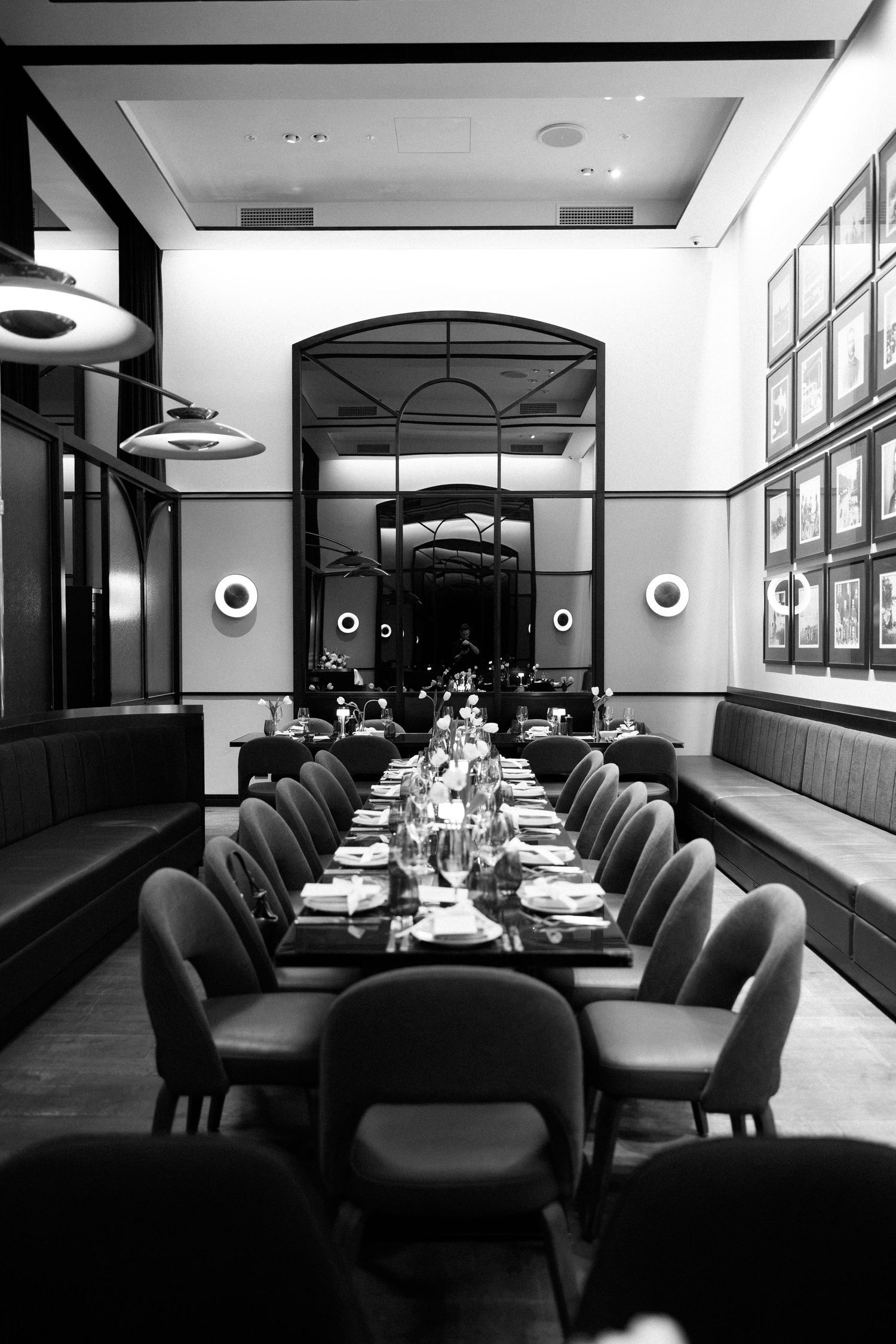 Elegant black and white fine dining room with long table set for dinner, upholstered chairs, and arched mirror backdrop.