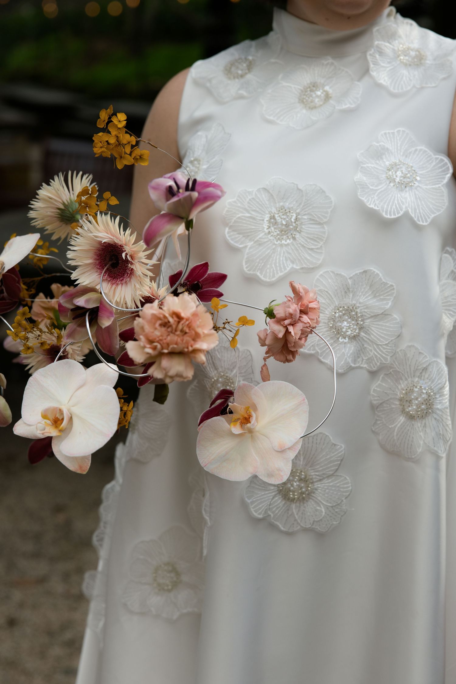 Bride in white floral applique gown holding a modern wedding bouquet with orchids, pink blooms, and burgundy accents.