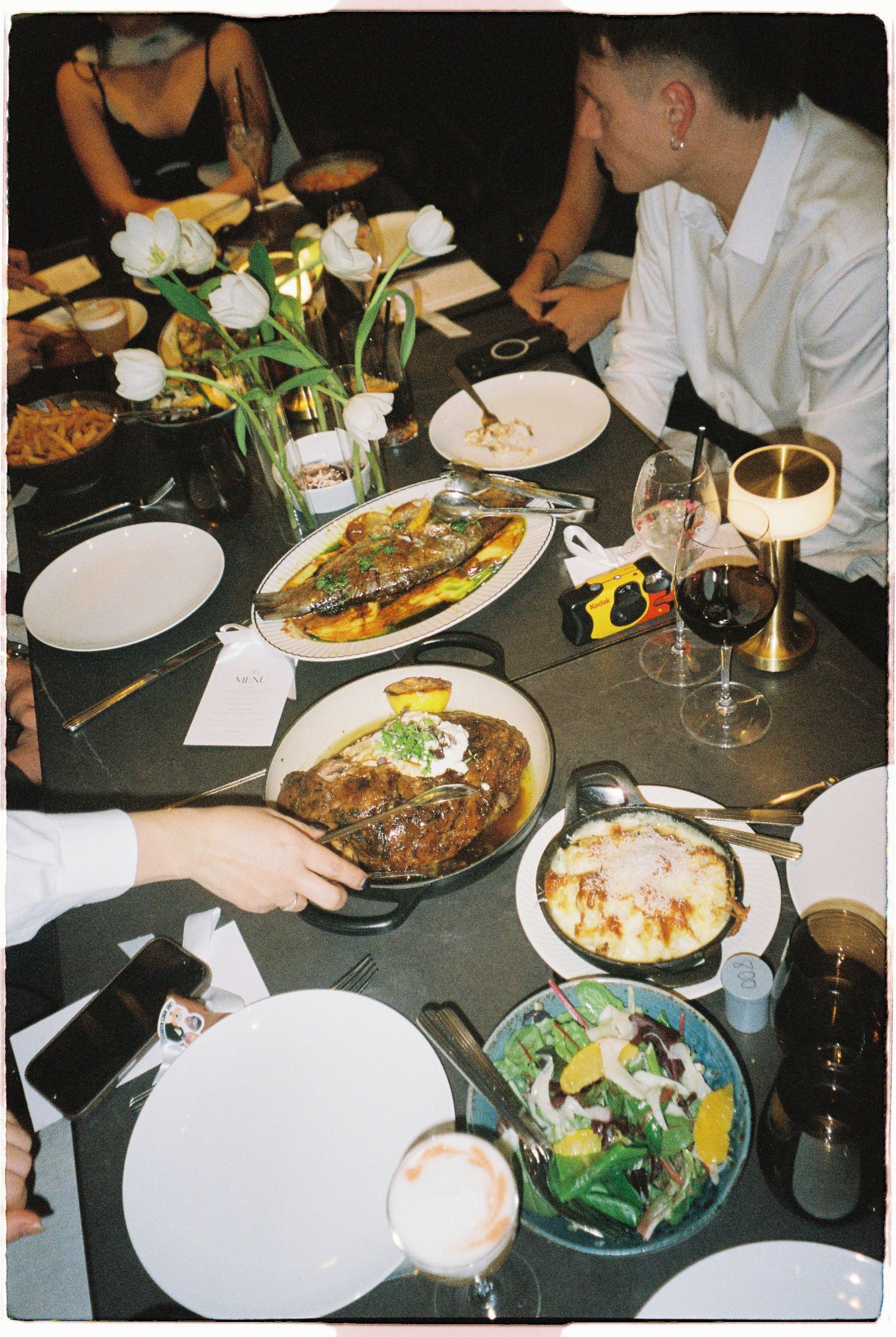 Elegant dinner table spread with whole fish, steak, salad and wine glasses at upscale restaurant celebration.
