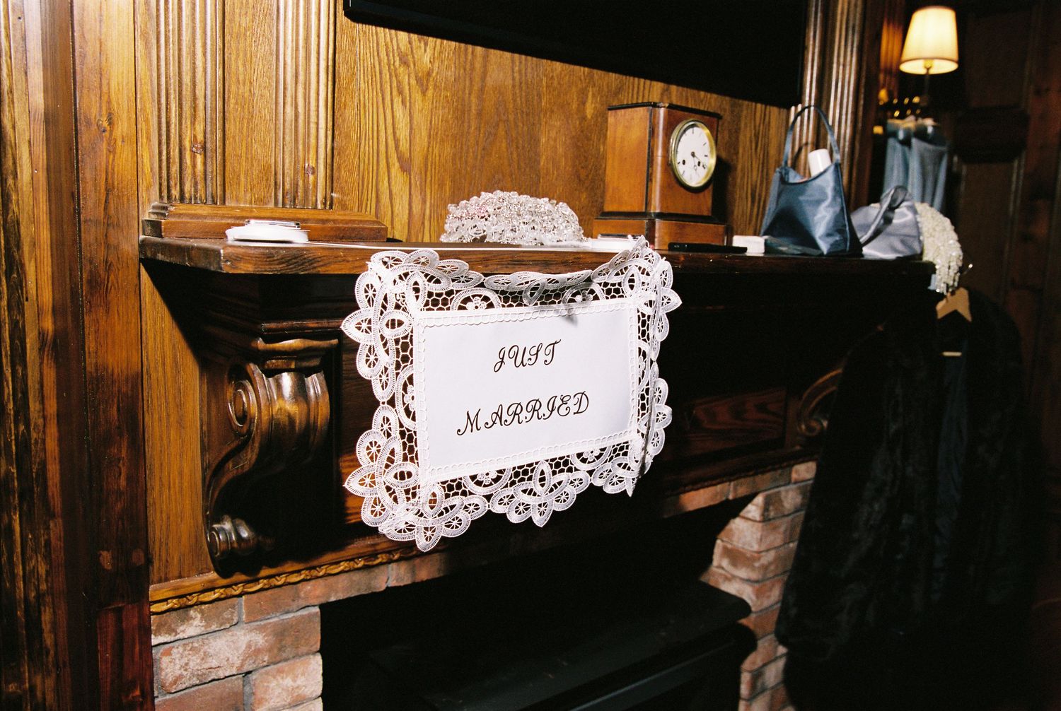 Just Married sign displayed on ornate wooden fireplace mantel with clock and accessories.