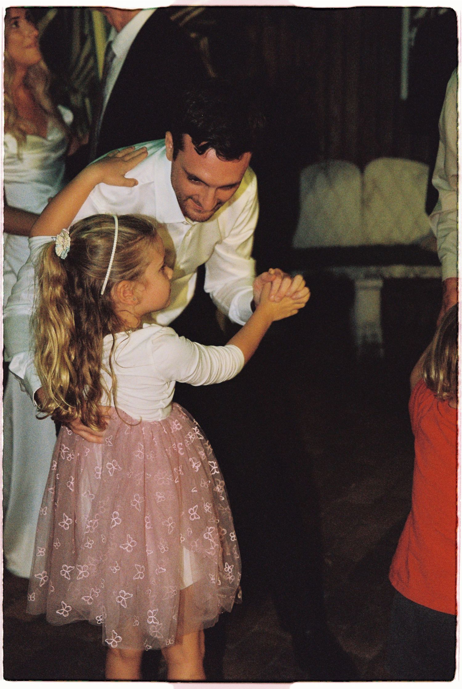 Father in white shirt dancing with young girl in pink tulle skirt at wedding.