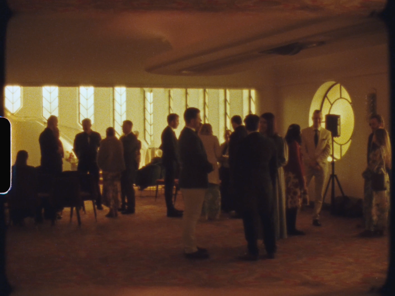 Group of people gathered in a warmly lit interior space with decorative windows during a social event.