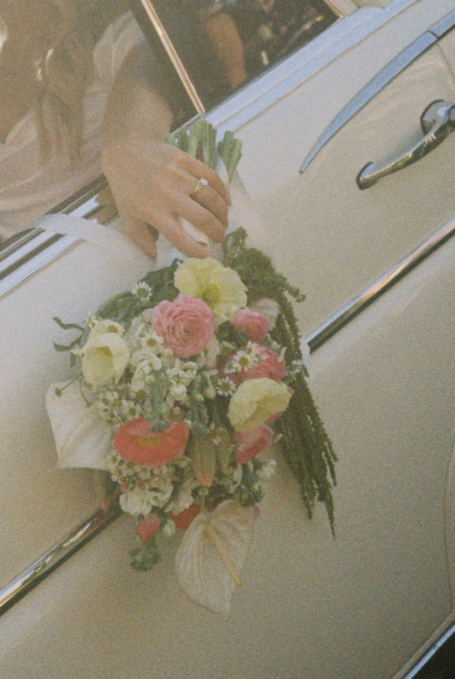 A bridal bouquet of pink, white, and coral flowers rests on a vintage white car.