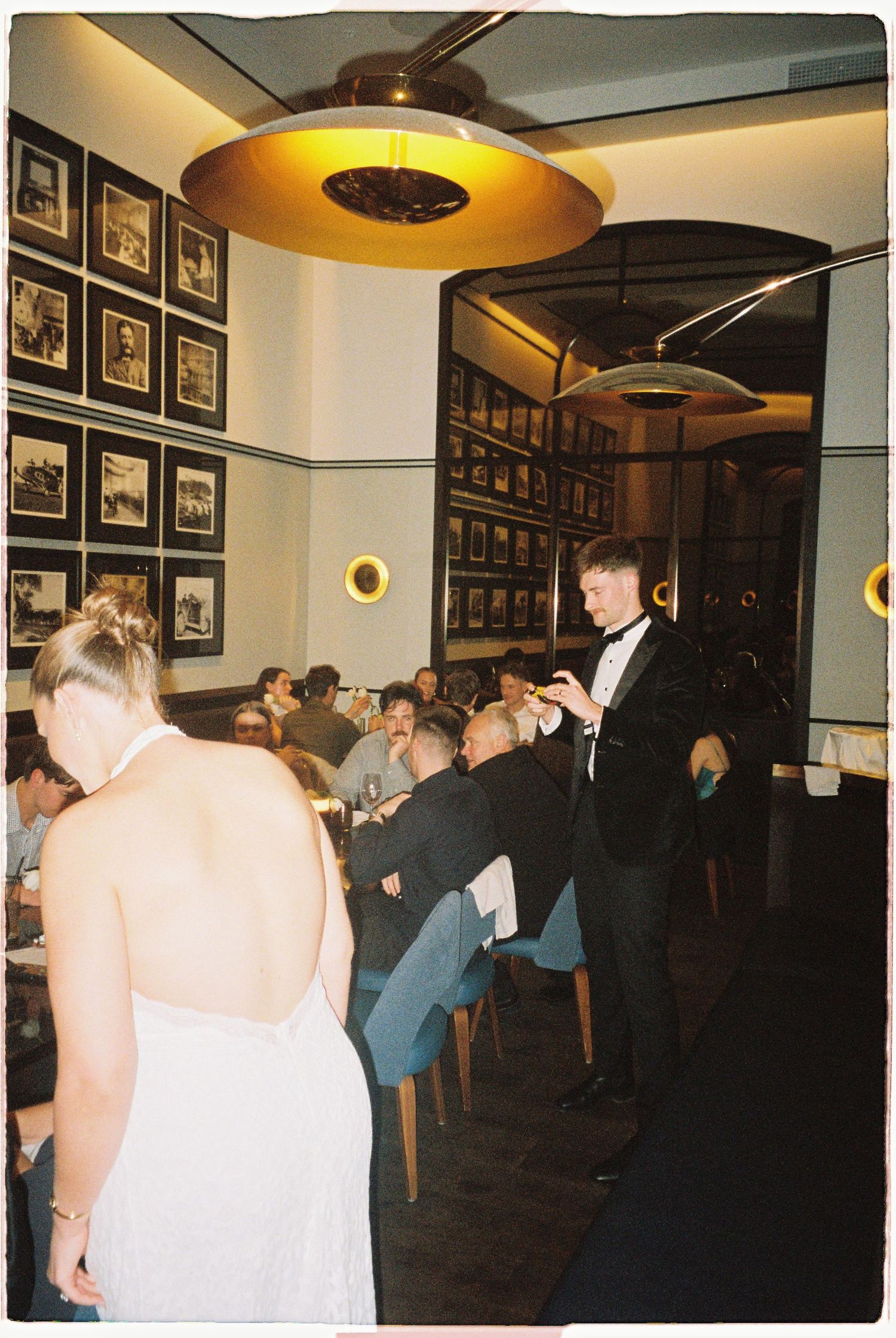 Groom in tuxedo stands near bride in elegant white dress during a sophisticated indoor wedding reception.