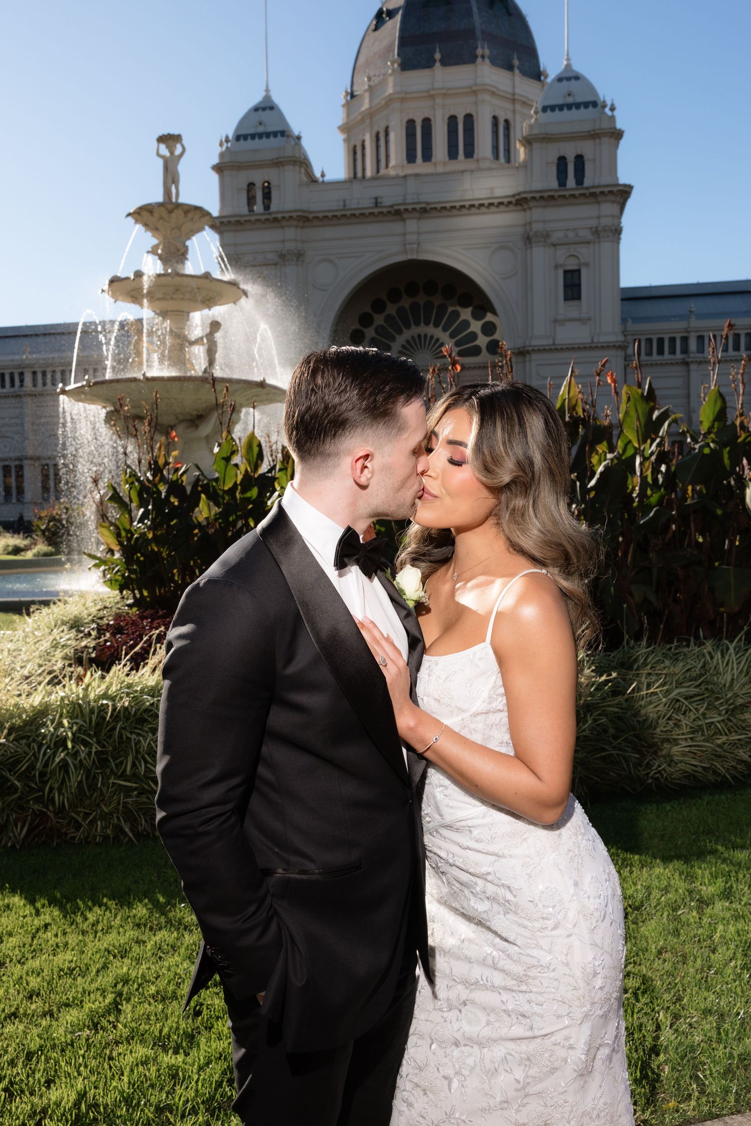 Bride and groom sharing a romantic kiss in front of an ornate historic building and fountain.