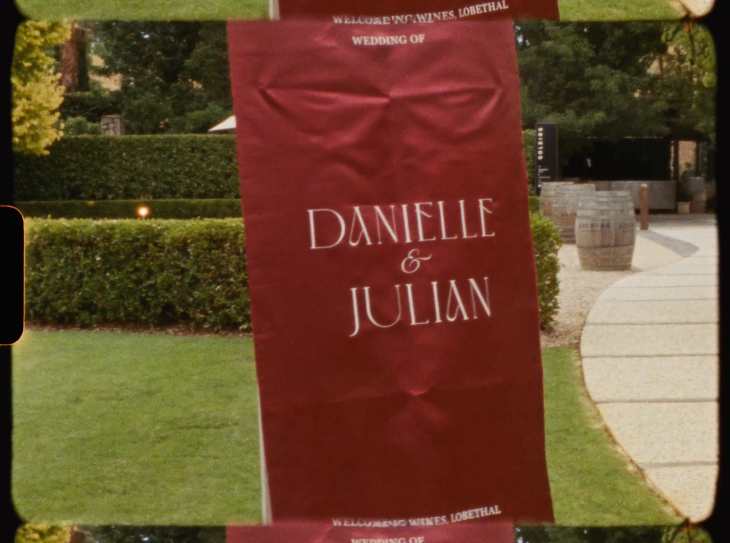 Red wedding banner sign reading Danielle and Julian displayed outdoors at wedding venue.