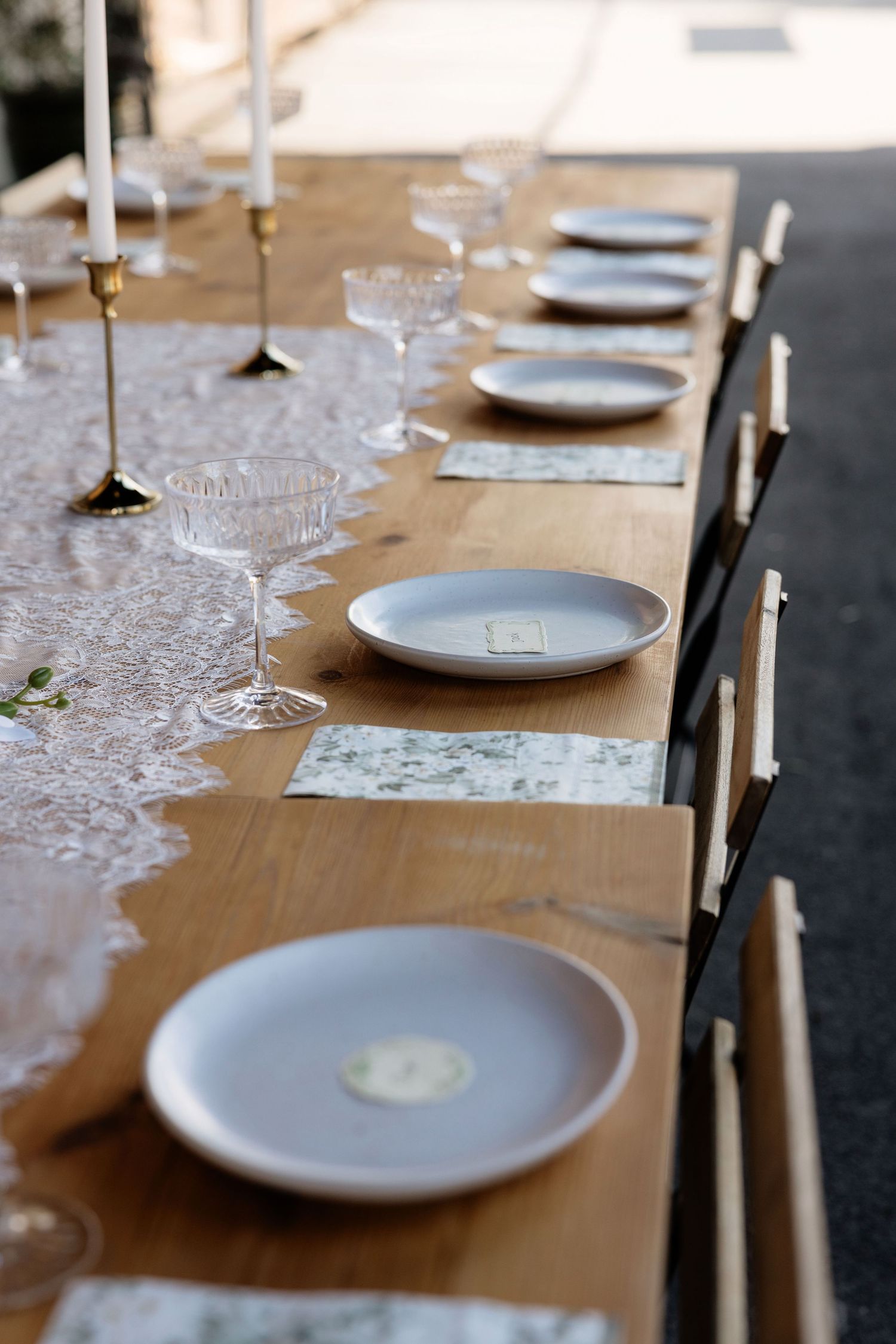 Elegant wedding reception table set with crystal glassware, white plates, and gold candlesticks on wood.