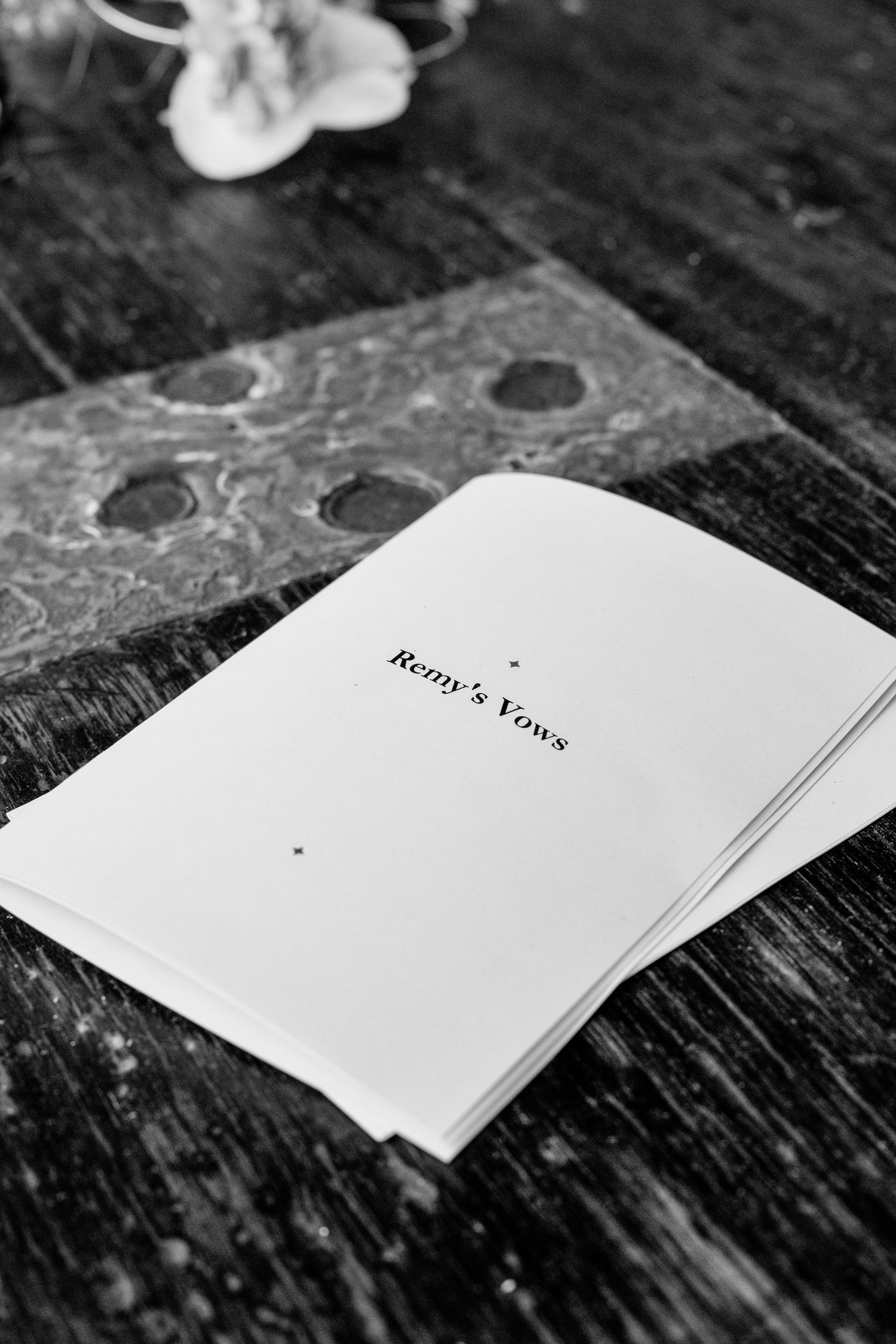 Black and white photo of Remy's wedding vows booklet resting on a rustic wooden table.