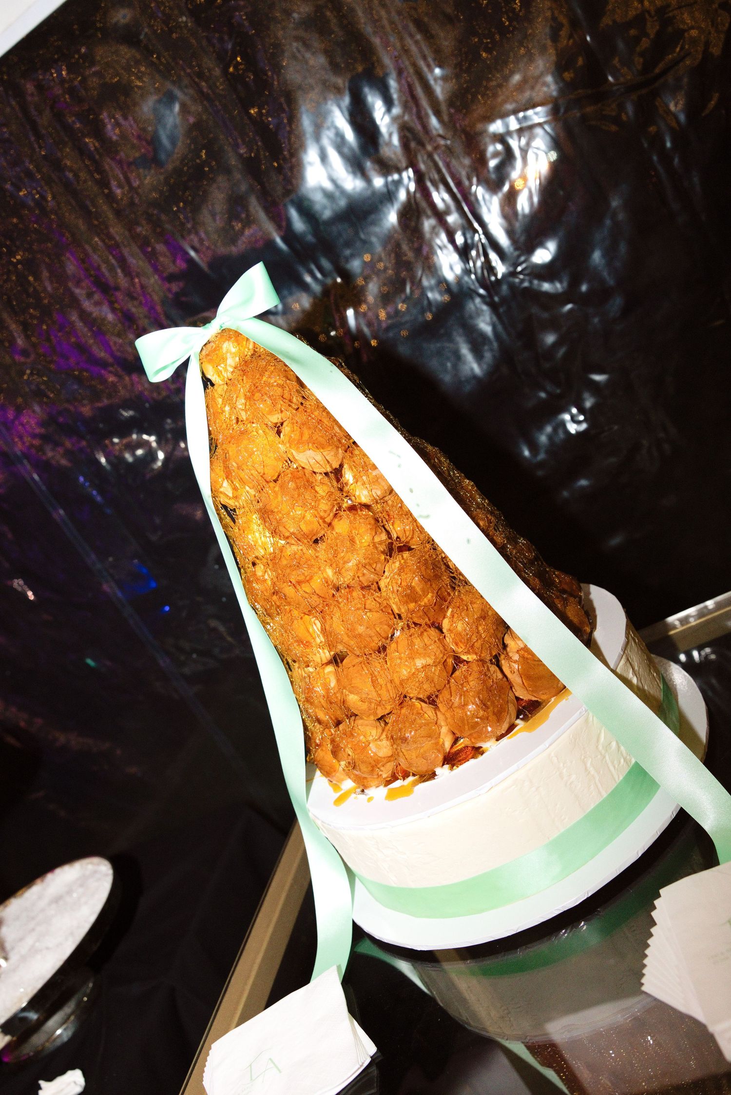 Elegant croquembouche wedding cake tower decorated with mint green ribbon bow on a white cake stand.