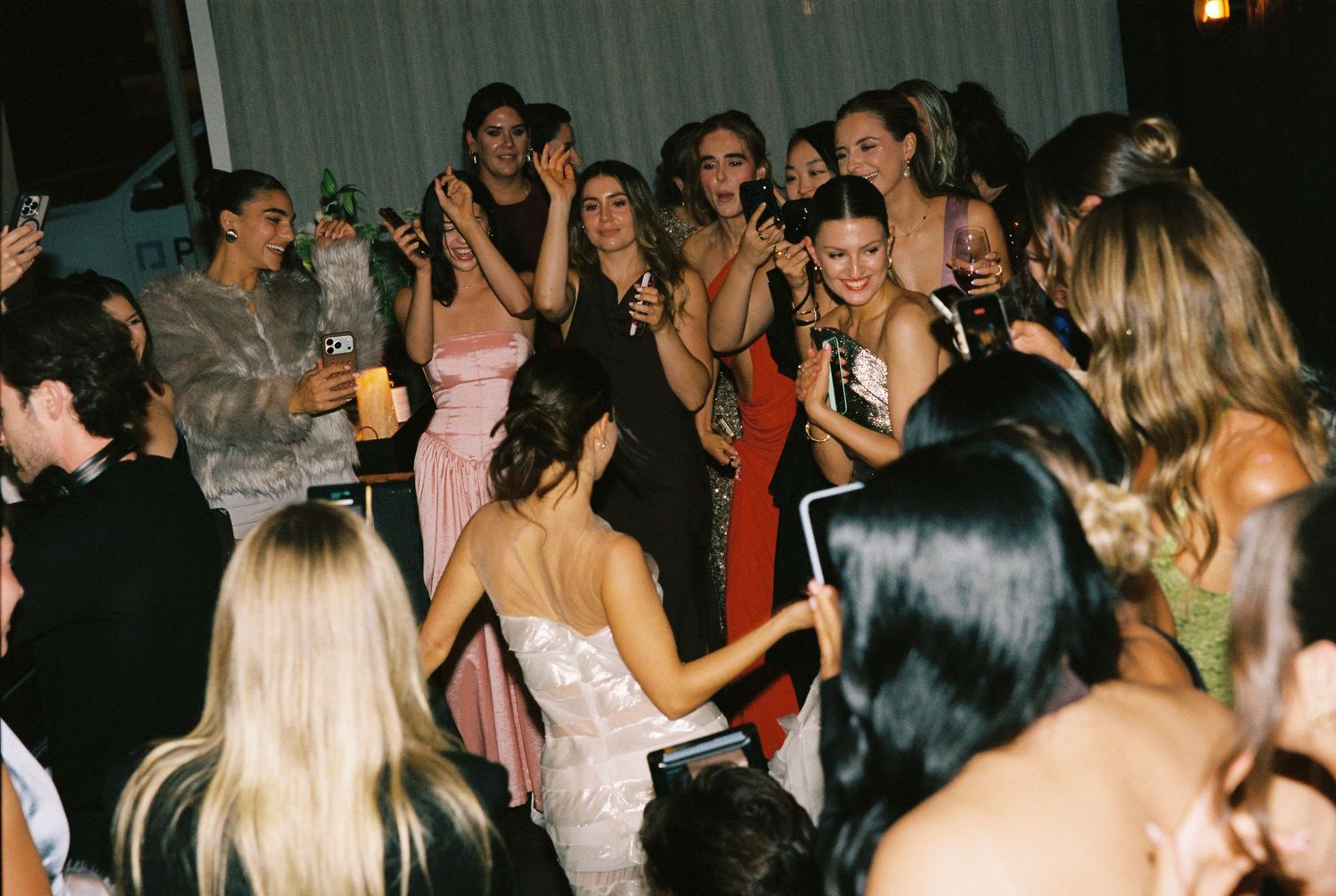 Bride surrounded by excited female guests dancing and celebrating at wedding reception.