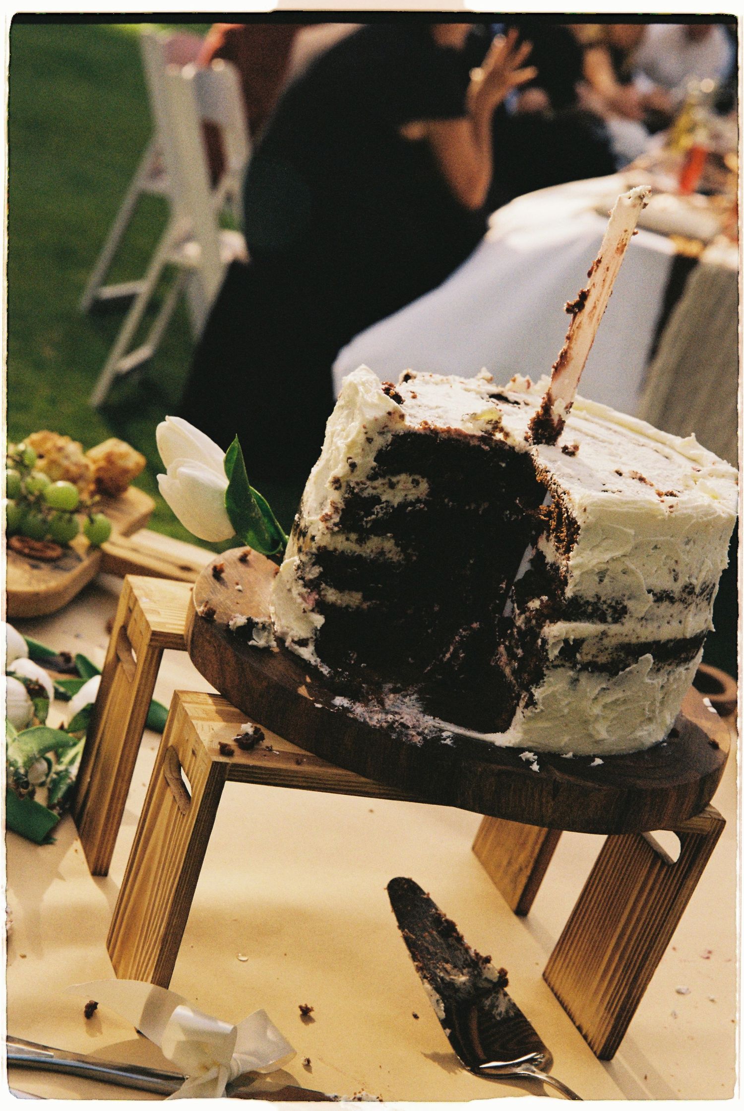 Partially sliced chocolate wedding cake with white frosting displayed on a wooden stand.