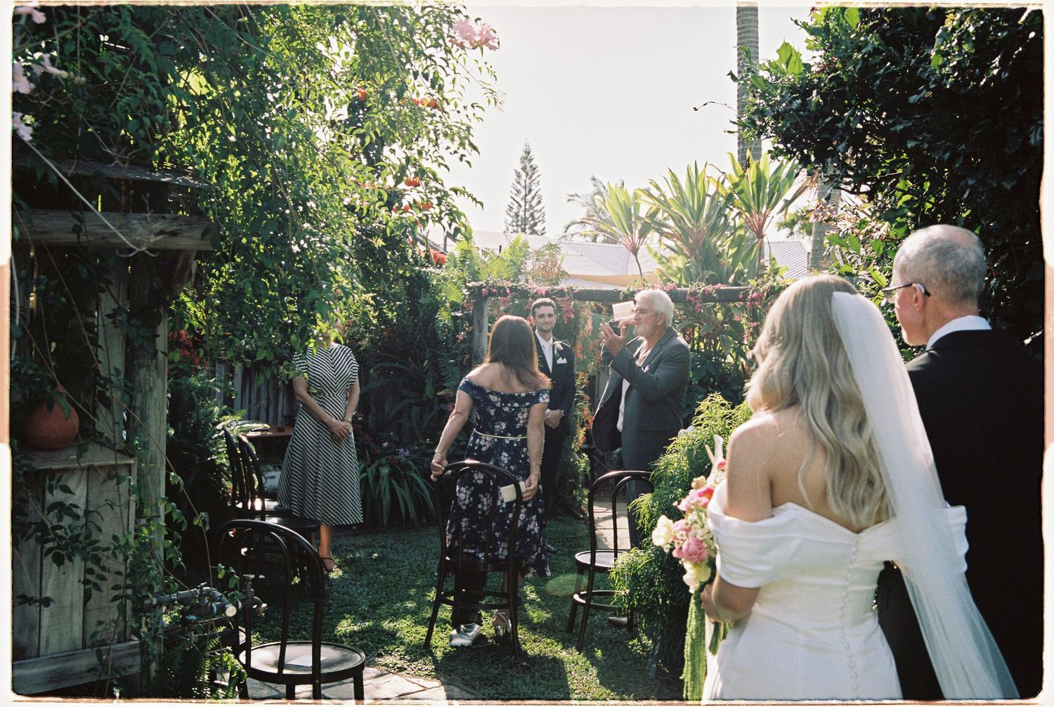 Small intimate outdoor garden wedding ceremony with guests seated as bride walks down the aisle.
