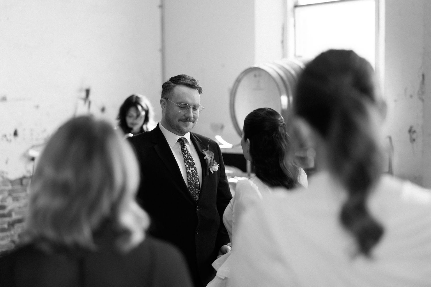 Groom smiling at bride during intimate winery wedding ceremony captured in black and white.