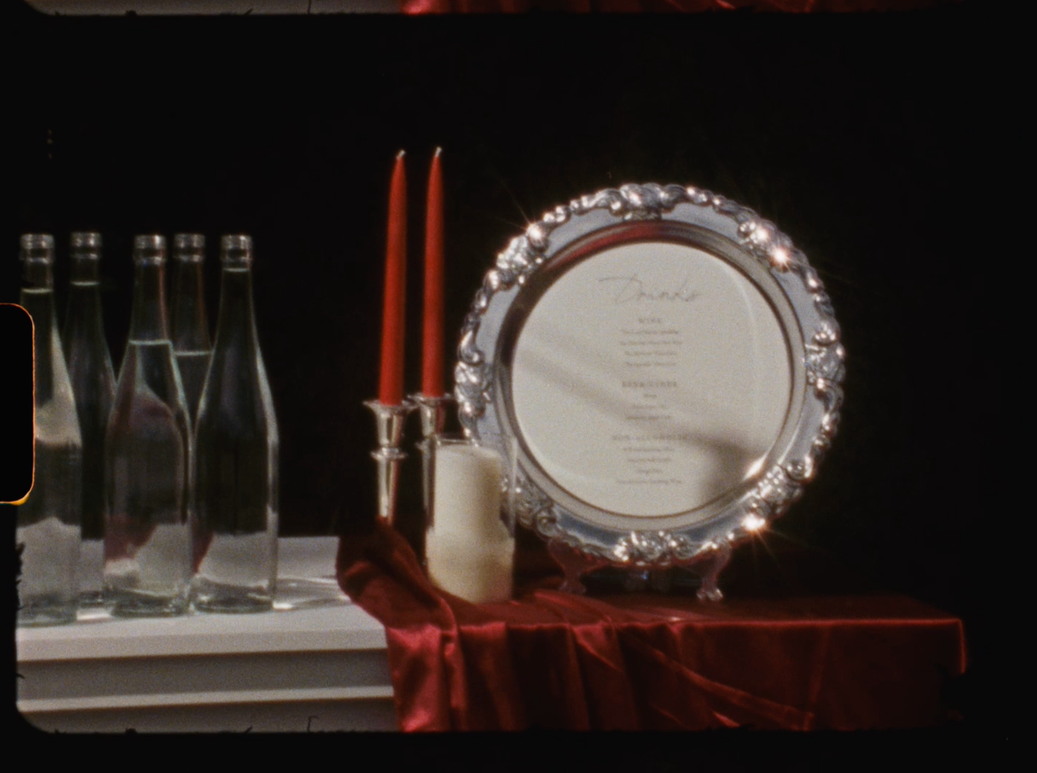 Elegant silver decorative plate with red candles and glass bottles on red velvet wedding table display.